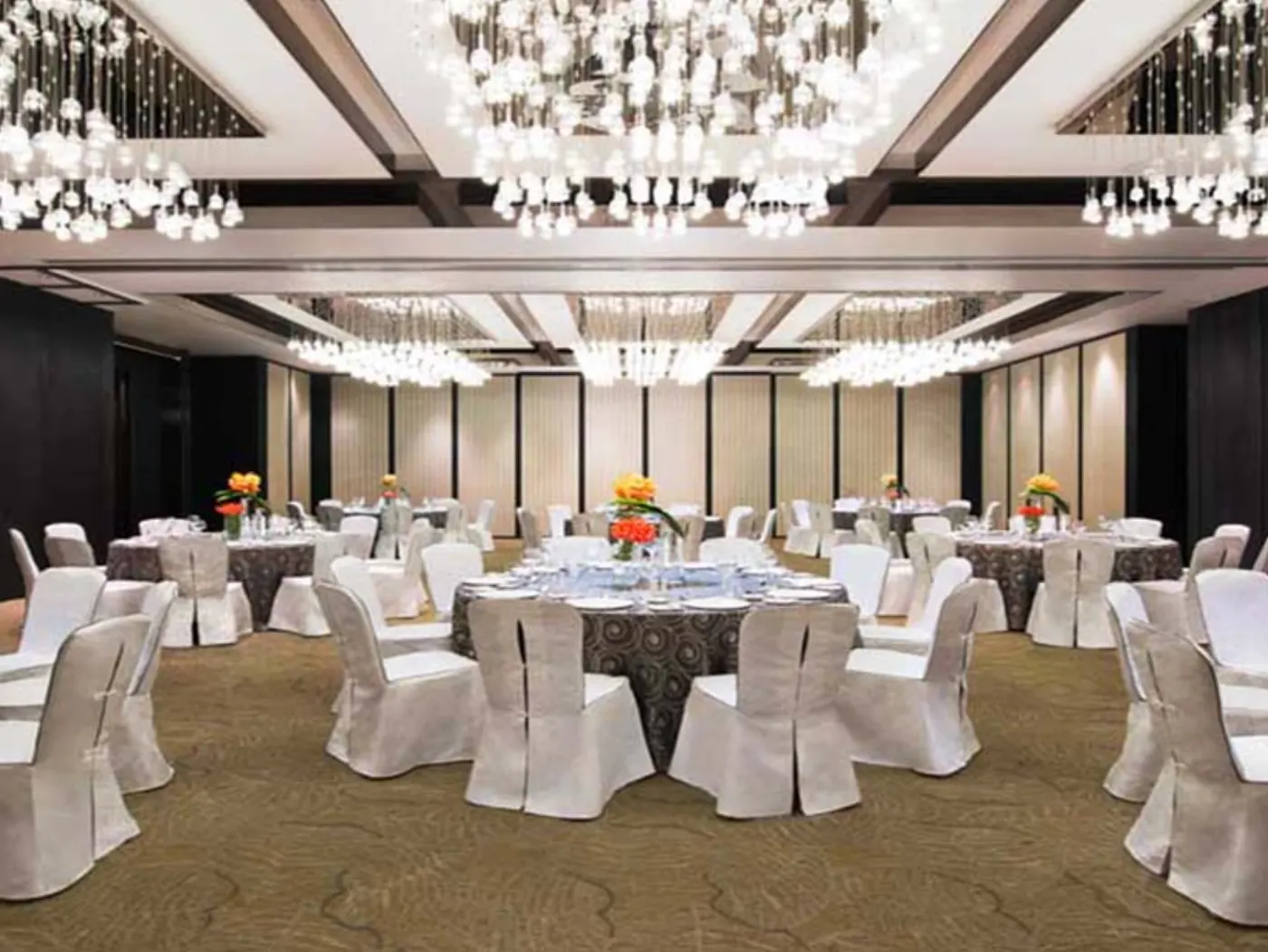 Salle de banquet aux lustres de cristal, tables rondes dressées et housses blanches sur les chaises