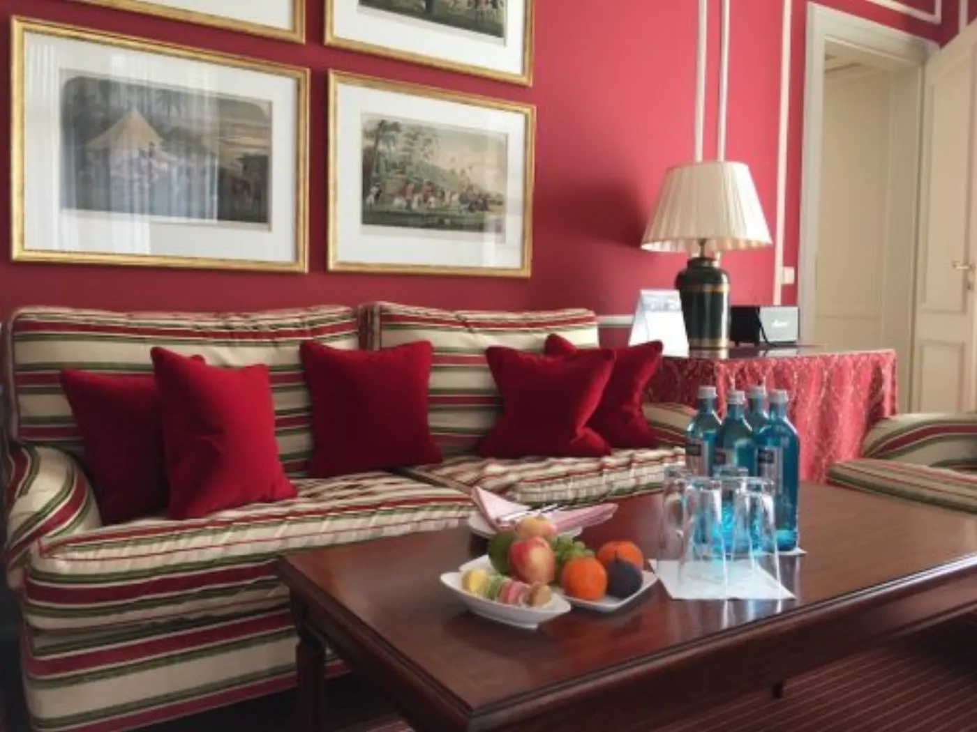 Salon de suite aux murs framboise : canapé rayé, gravures encadrées et corbeille de fruits sur la table