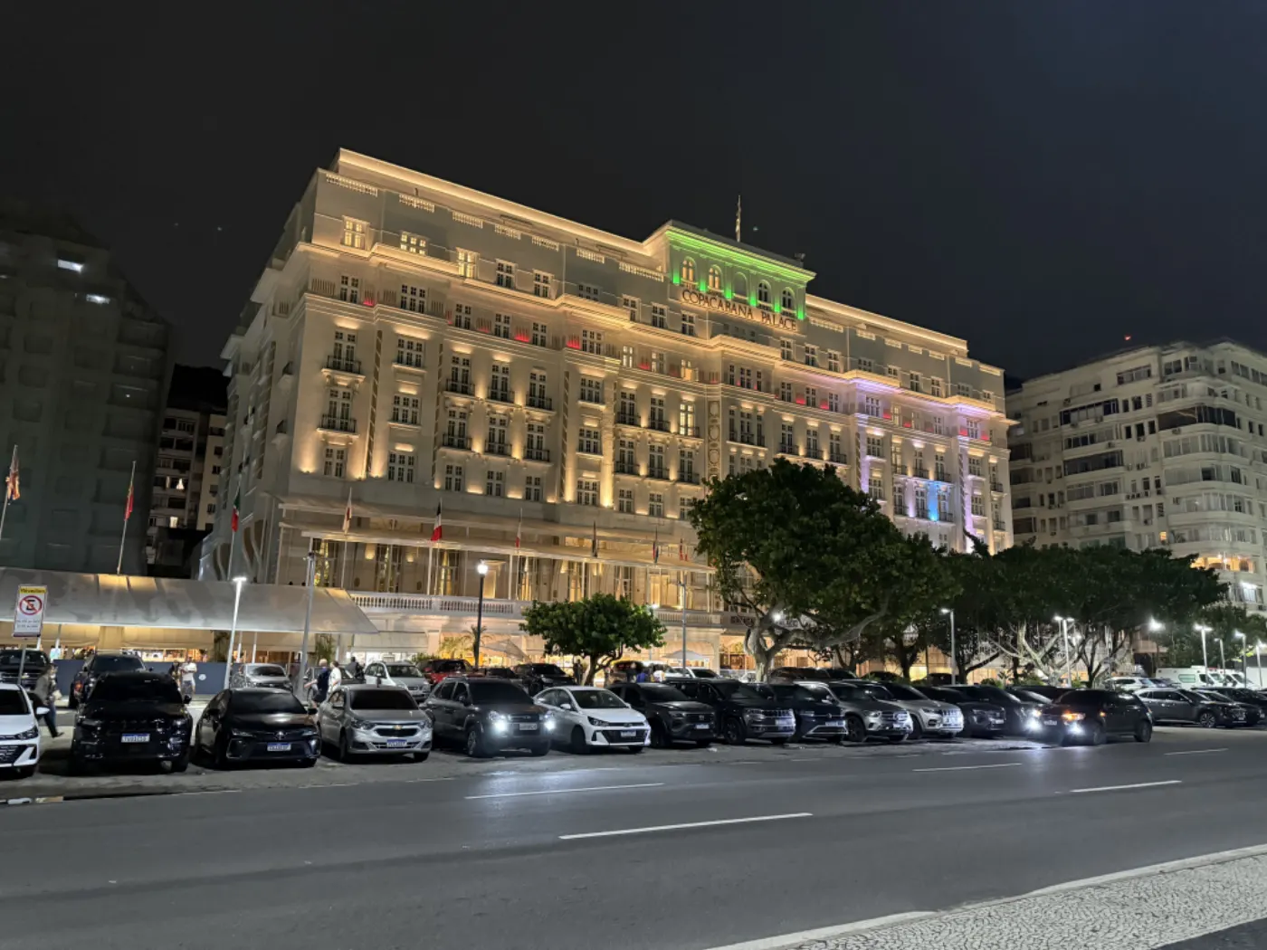 Le Copacabana Palace illuminé la nuit, vu depuis l'avenue bordée de voitures en stationnement