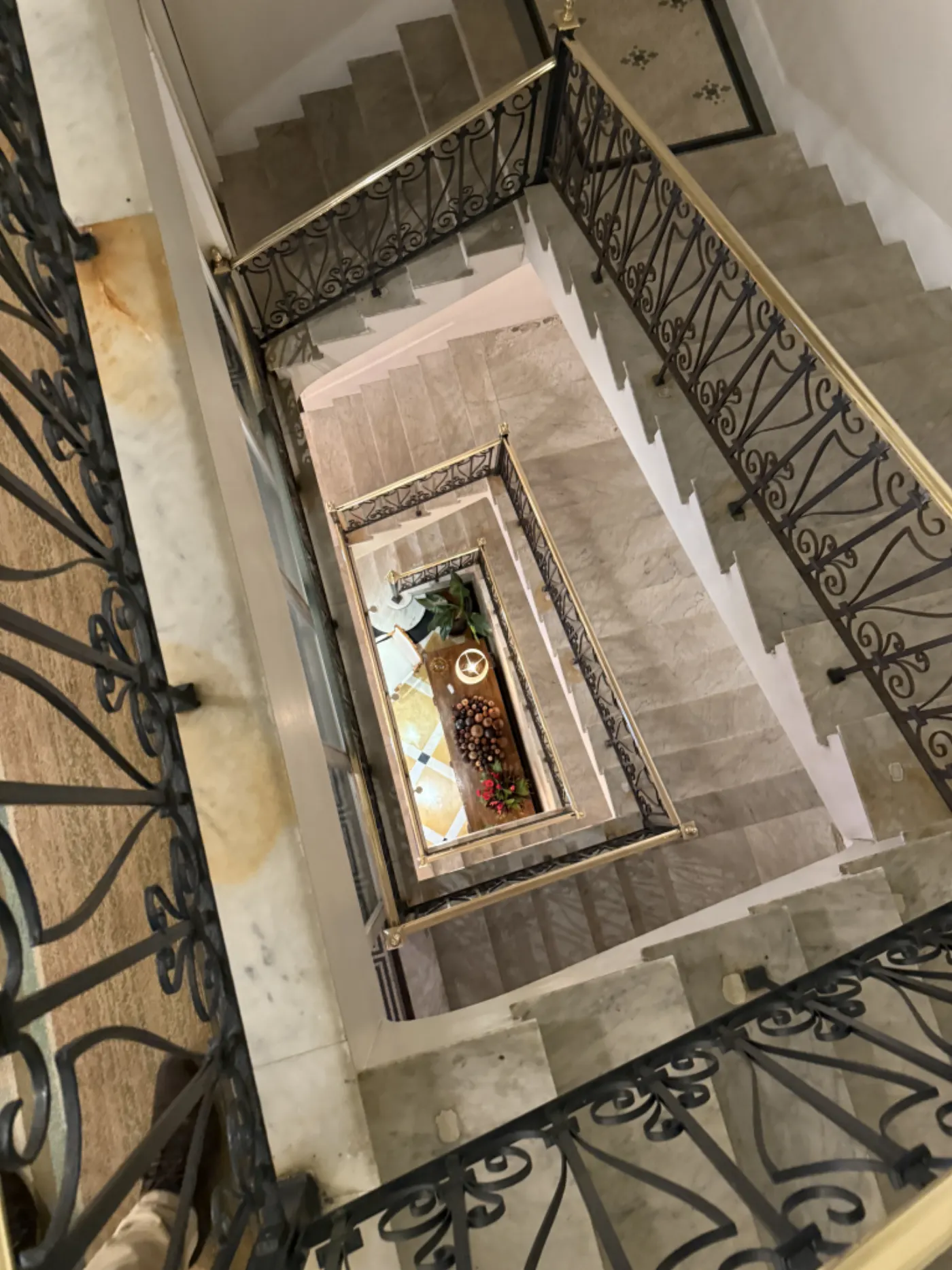 Cage d'escalier vue en plongée, marches de marbre et rampes en fer forgé s'enroulant jusqu'au hall