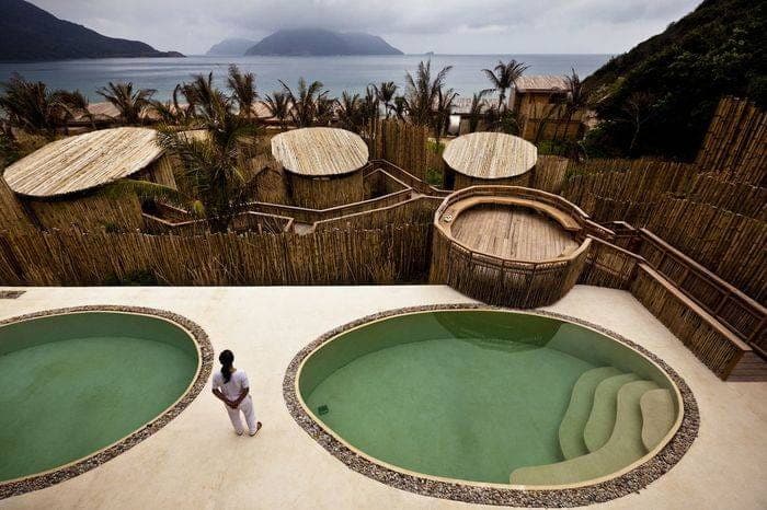 Bassins ronds d'un spa en bord de mer, paravents de bambou et toits ronds face aux montagnes