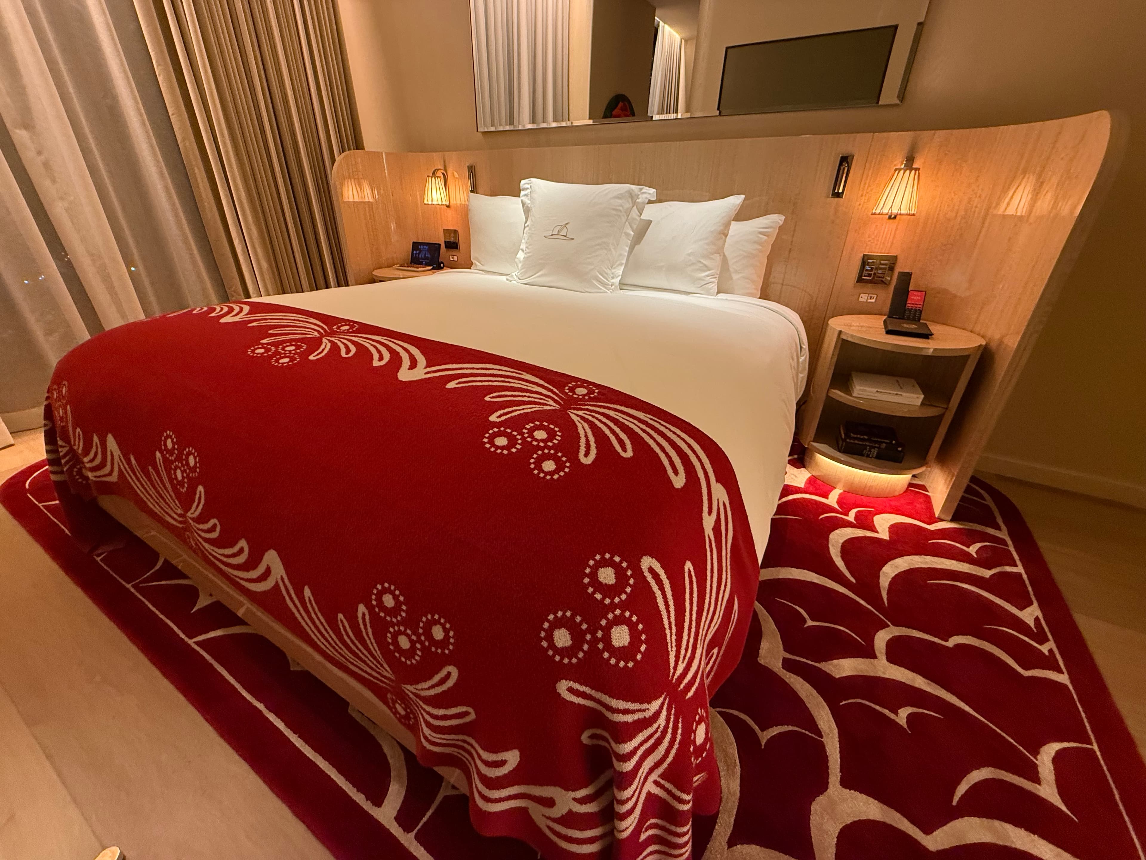 Chambre du Faena New York : couvre-lit et tapis à motifs rouge et blanc, tête de lit en bois courbé