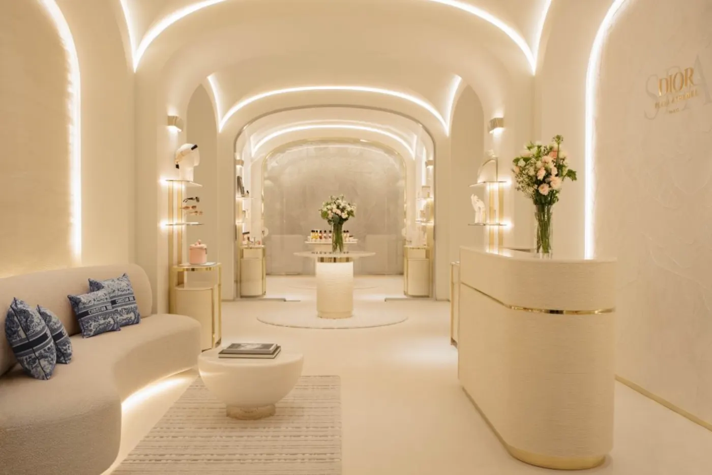 Réception du Spa Dior, voûtes crème éclairées, comptoir laqué, coussins toile de Jouy et bouquet de roses