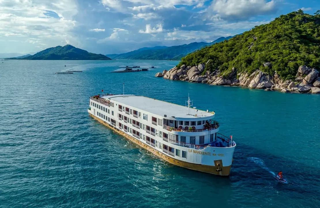 Le bateau de croisière La Marguerite au mouillage dans une baie turquoise bordée d'îles boisées