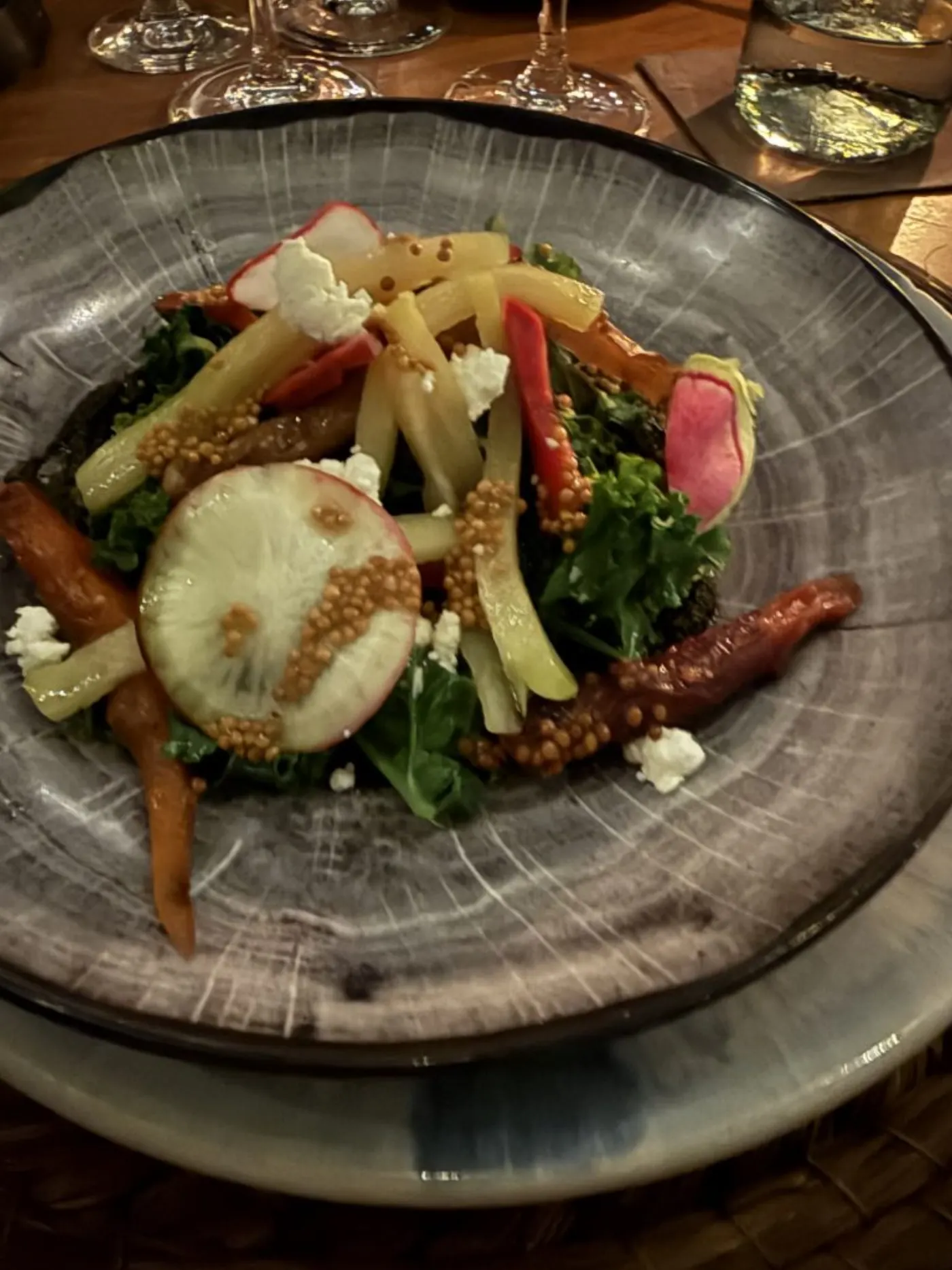 Assiette sombre garnie de jeunes pousses, carottes glacées, radis, graines de moutarde et éclats de fromage frais
