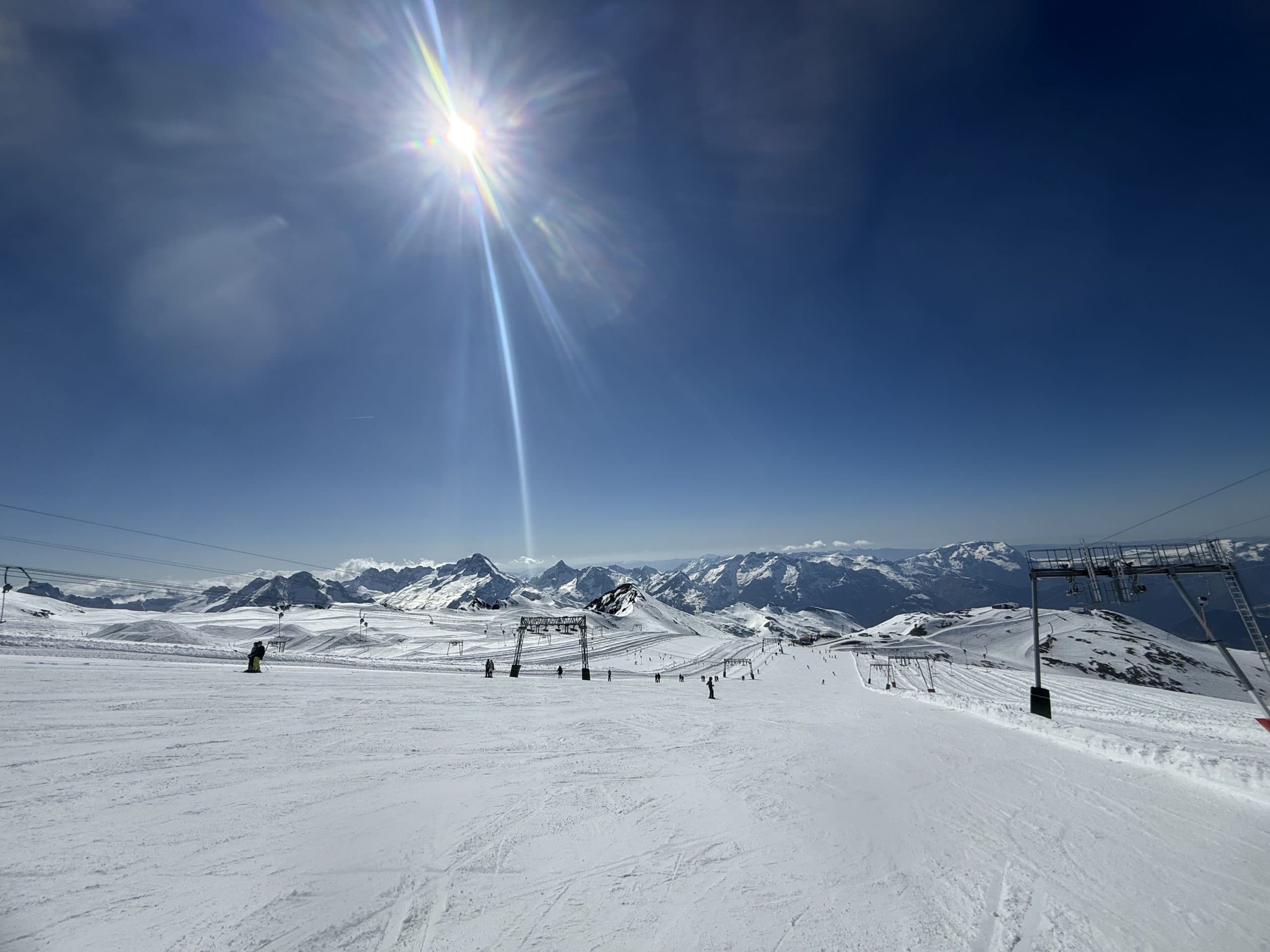 Piste de ski enneigée sous le soleil, télésièges et sommets alpins à l'horizon