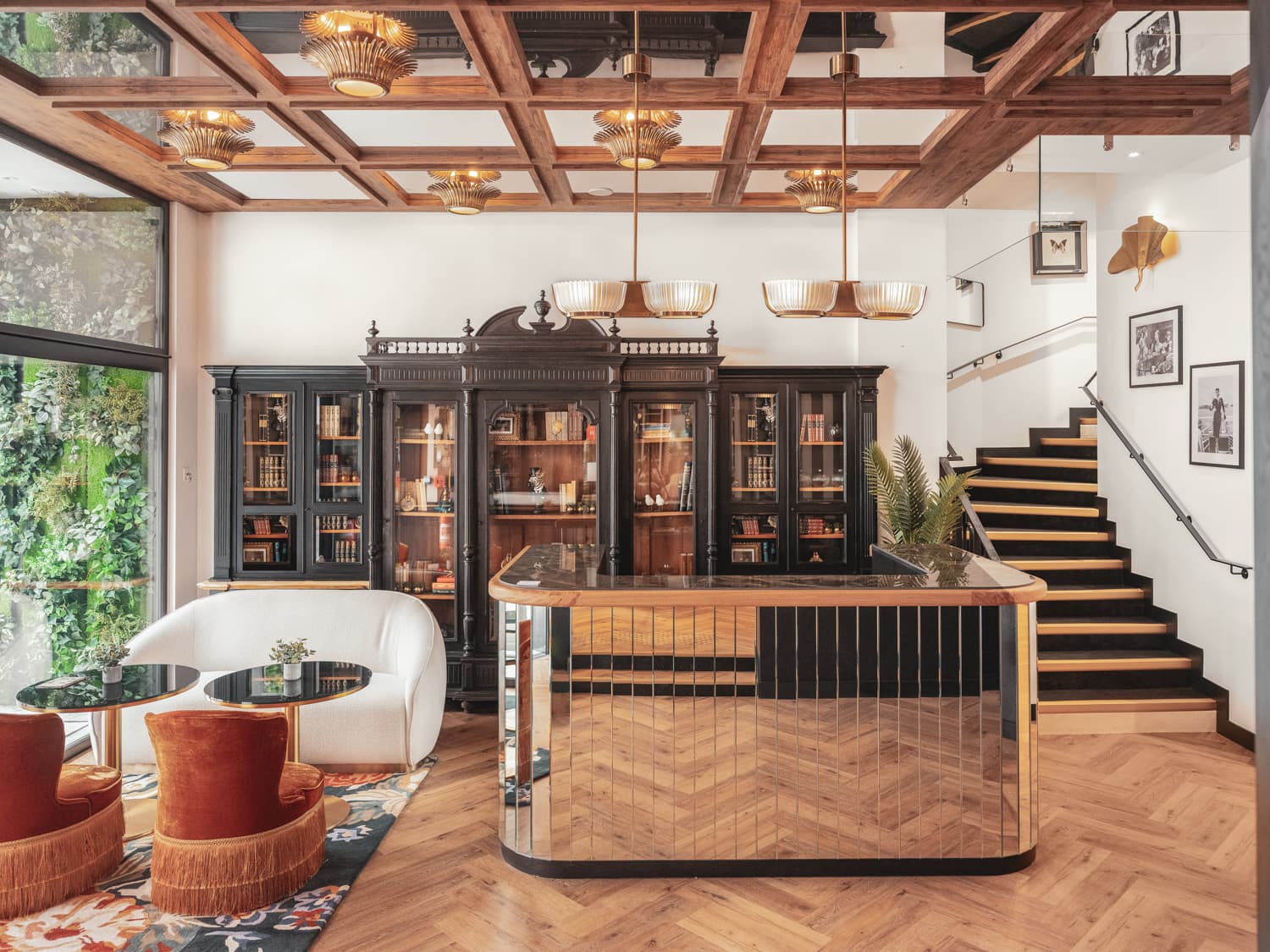 Réception d'hôtel au comptoir miroir, plafond à caissons de bois, bibliothèques noires et fauteuils de velours orange