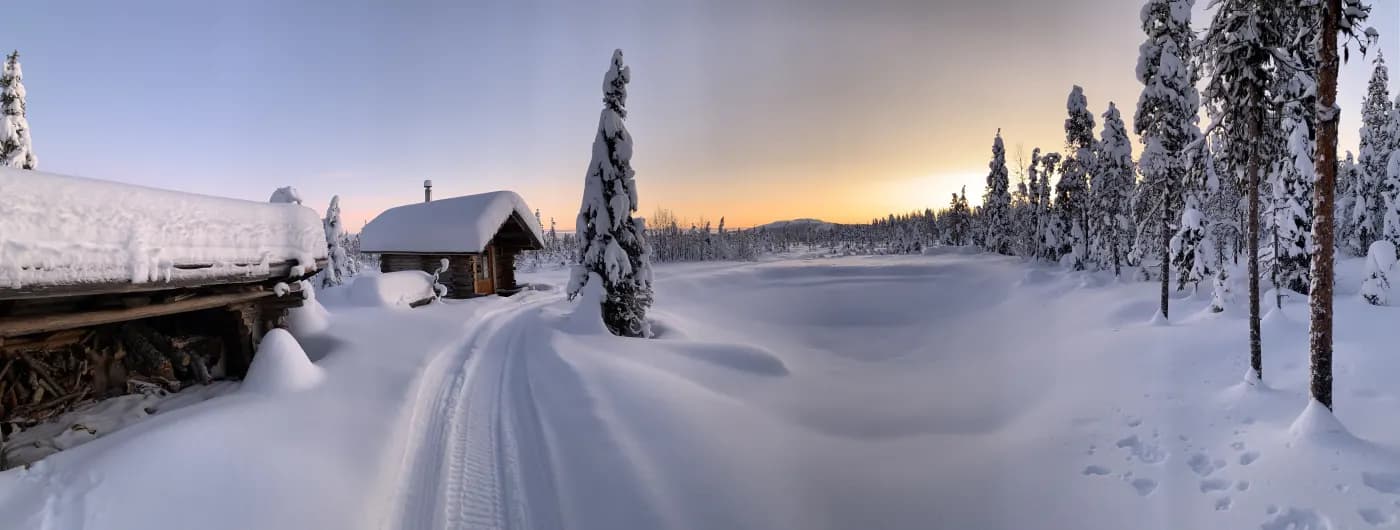 Paysage enneigé au coucher du soleil, petit chalet en rondins sous la neige et trace de ski entre les sapins