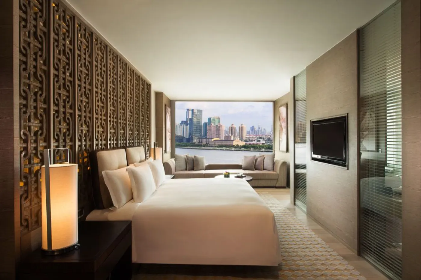 Chambre au paravent chinois ajouré, lit king et baie vitrée ouverte sur les tours de Shanghai et la rivière