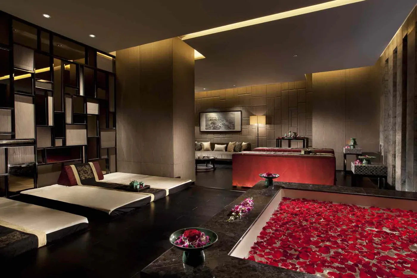 Suite spa aux lumières tamisées : bain rempli de pétales de rose rouges et deux tables de massage côte à côte