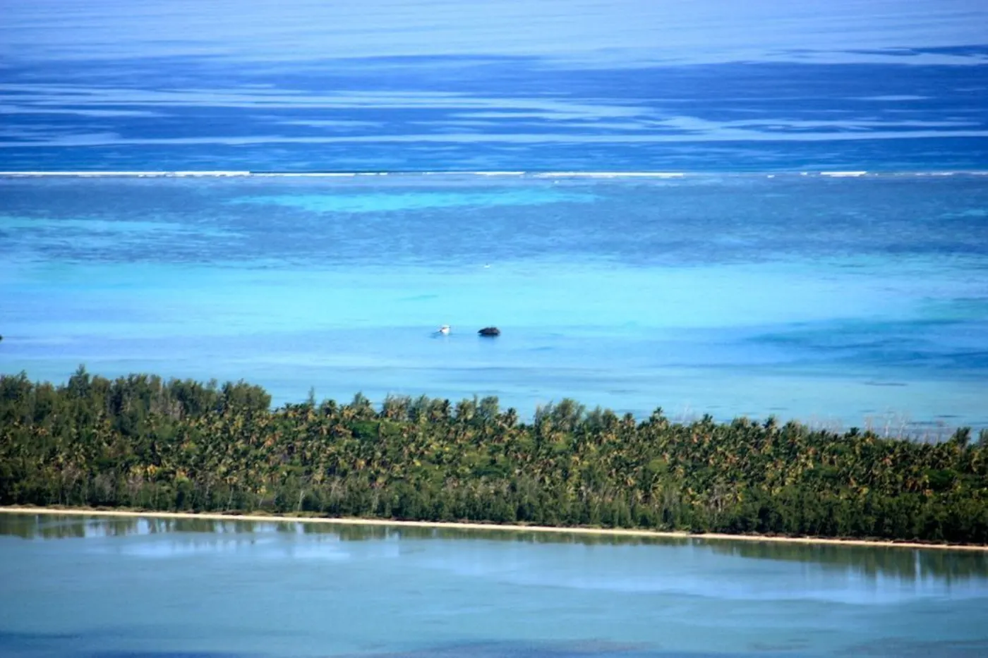 Lagon turquoise vu de hauteur, langue de terre plantée de cocotiers et ligne d'écume sur la barrière de corail