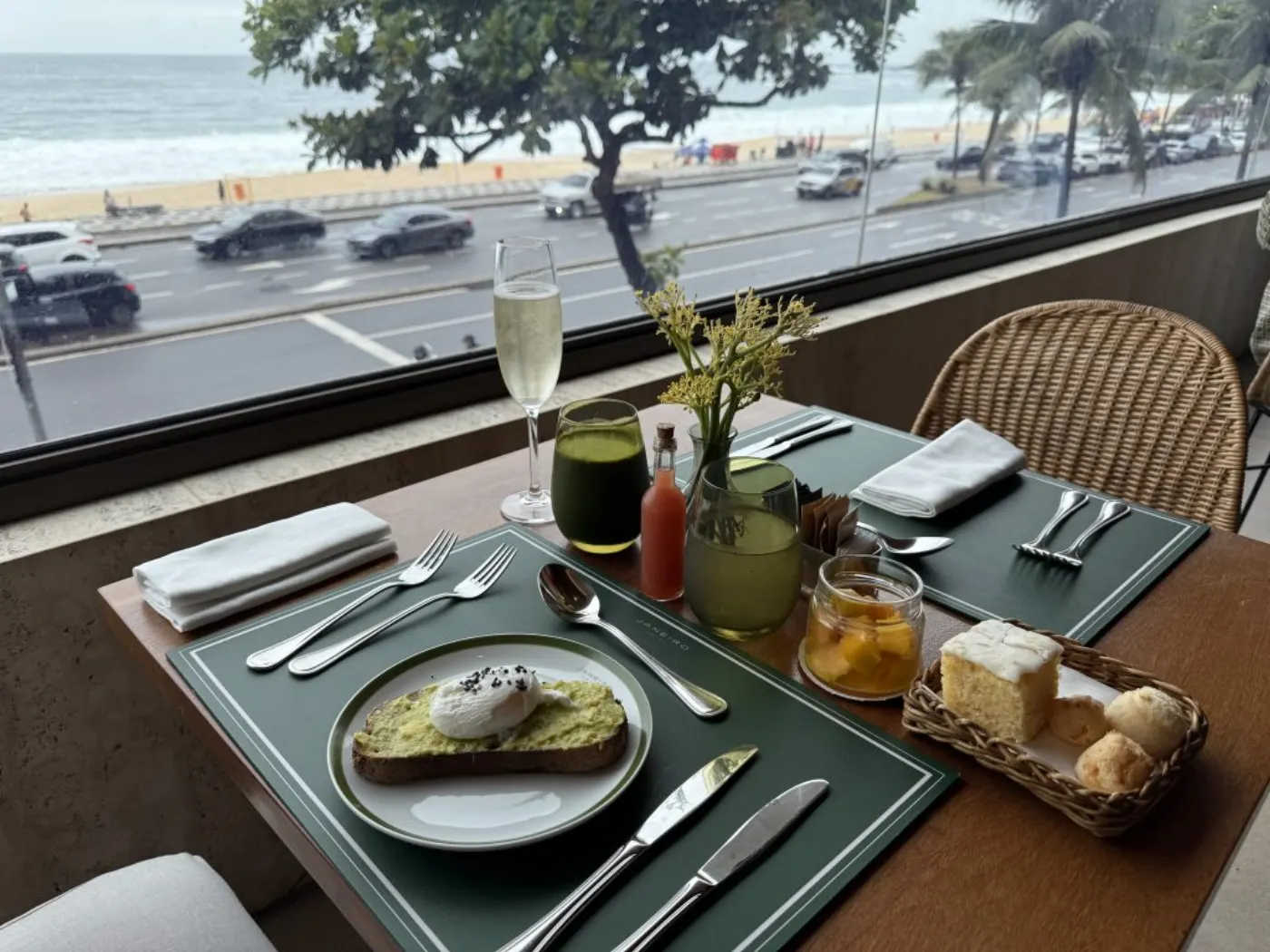 Petit-déjeuner dressé face à la plage : toast à l'avocat et œuf poché, jus vert et coupe de champagne