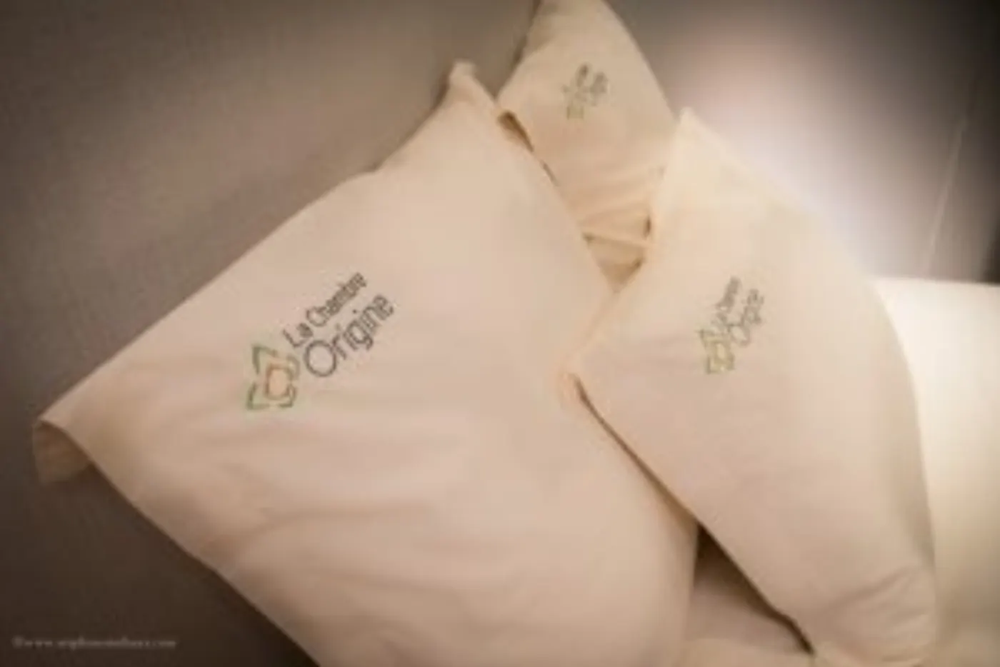Oreillers crème brodés du logo La Chambre Origine, posés sur un lit