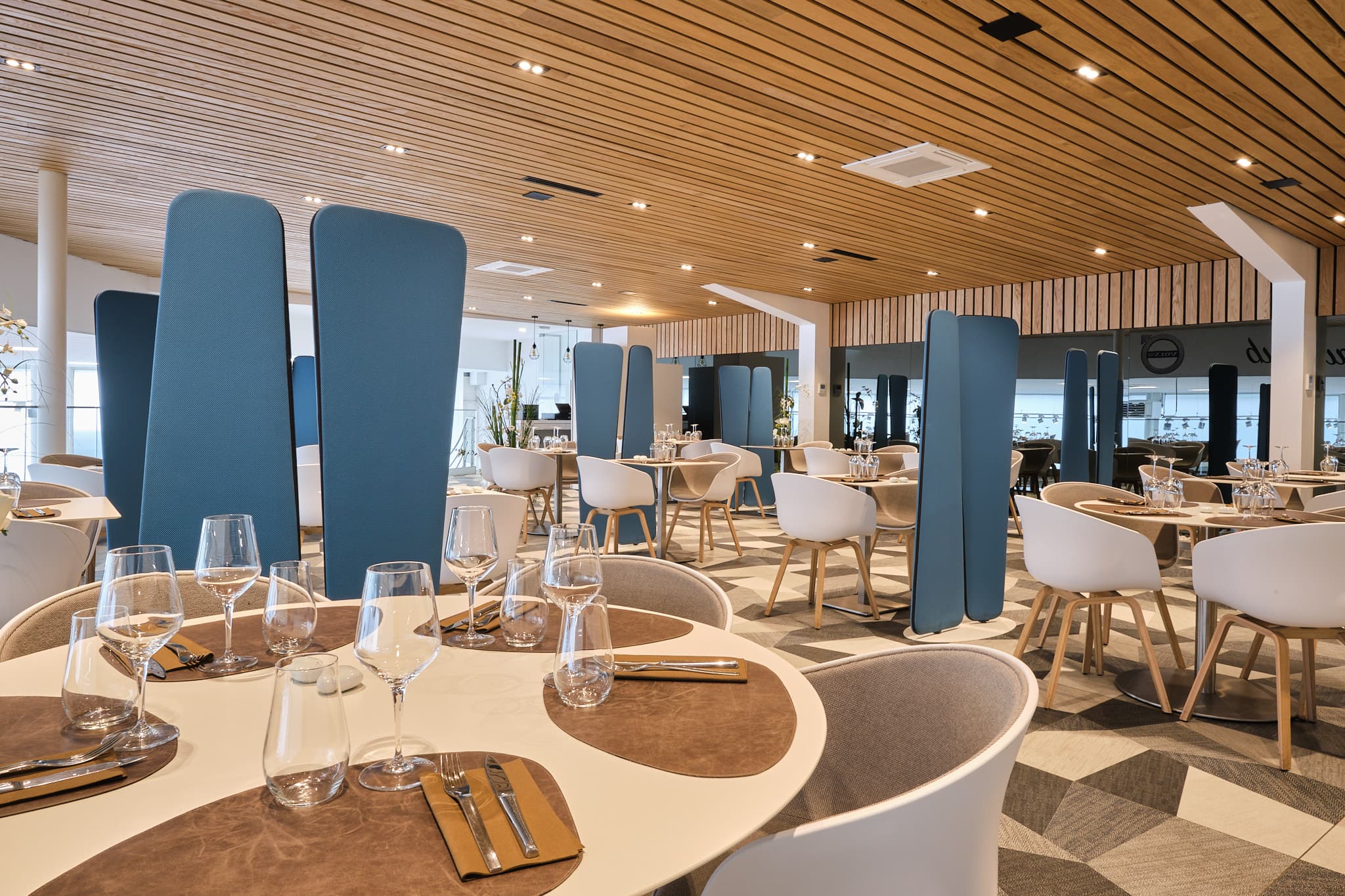 Salle de restaurant contemporaine : plafond de lattes de bois, paravents bleus et tables rondes dressées
