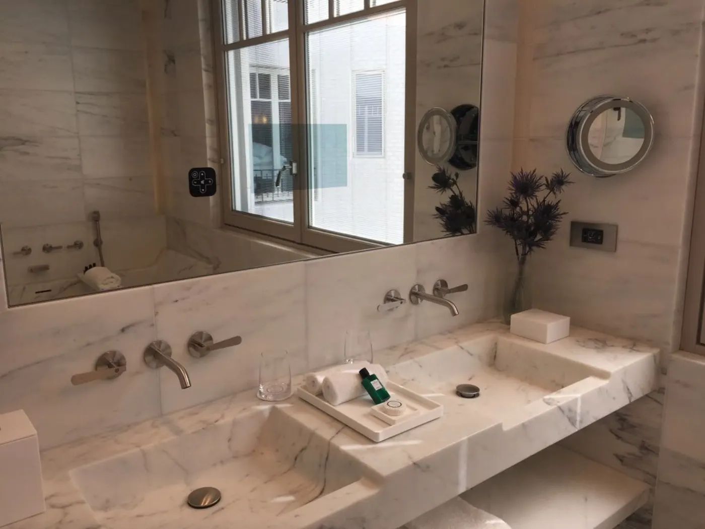 Salle de bains en marbre blanc du Lutetia, double vasque, robinetterie murale et miroir reflétant la baignoire
