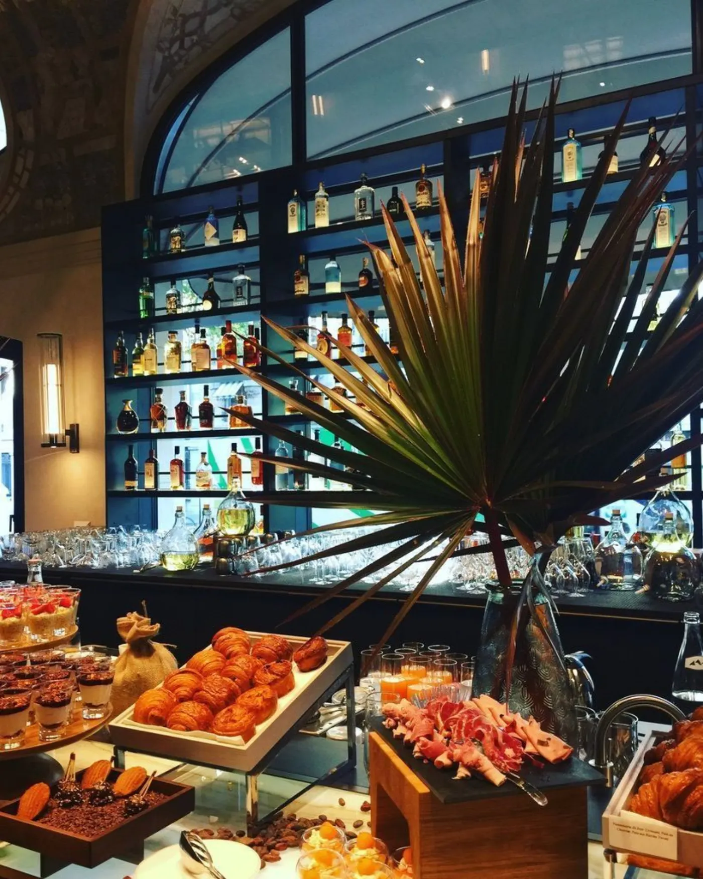 Buffet de petit-déjeuner (viennoiseries, charcuterie, verrines) devant le bar aux étagères de bouteilles rétroéclairées