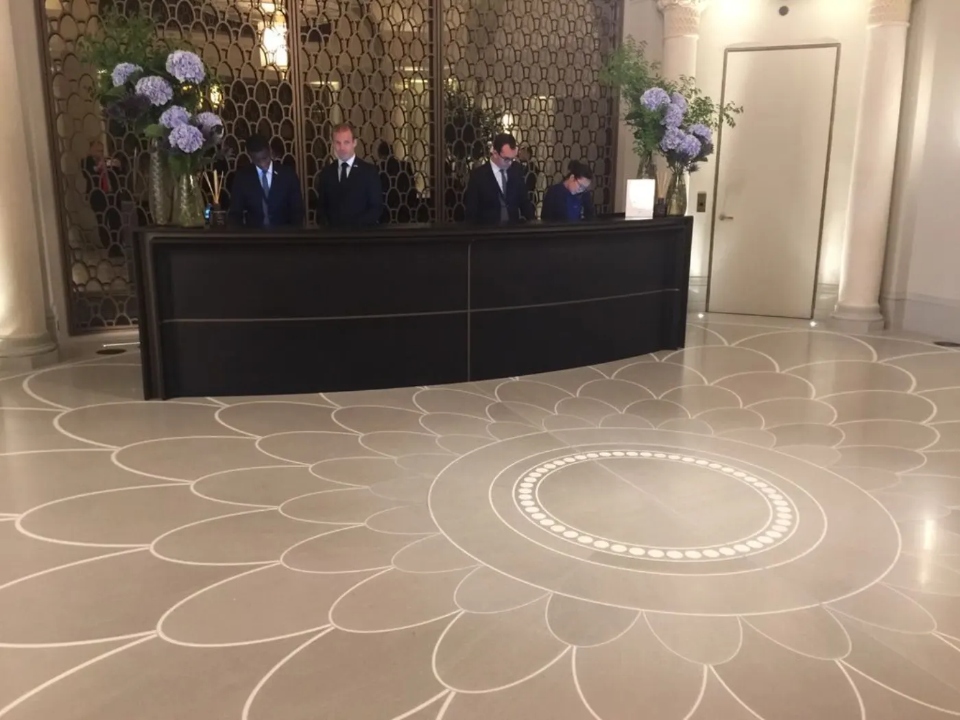 Quatre réceptionnistes en costume derrière le comptoir d'accueil, hortensias et sol en marbre à motif de pétales