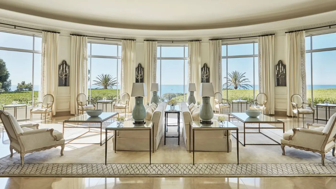 Grand salon ovale du Four Seasons Cap-Ferrat, canapés crème, lampes céladon et baies ouvertes sur la mer
