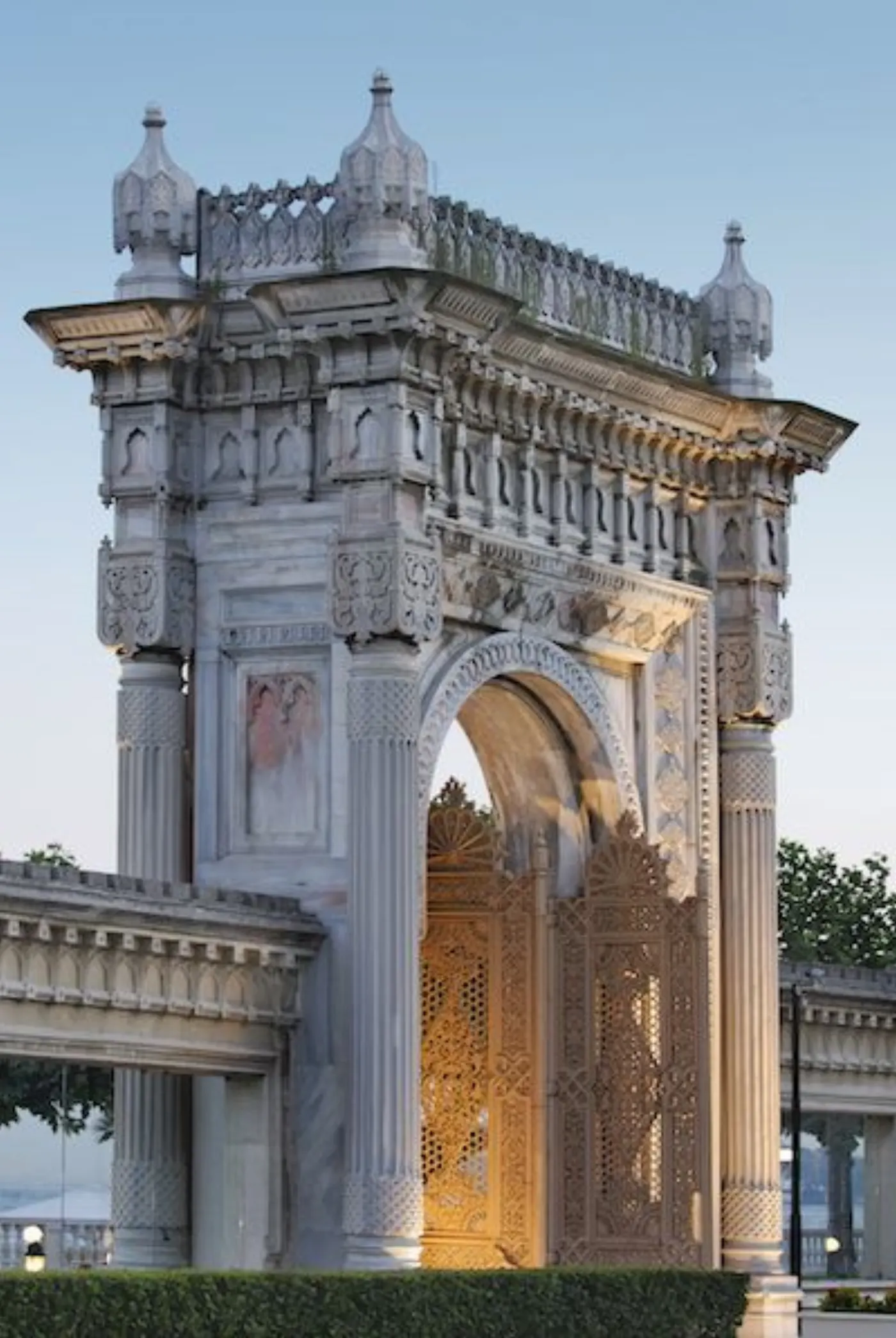 Porte monumentale en marbre blanc de style ottoman, arche sculptée et vantaux dorés ajourés, au crépuscule
