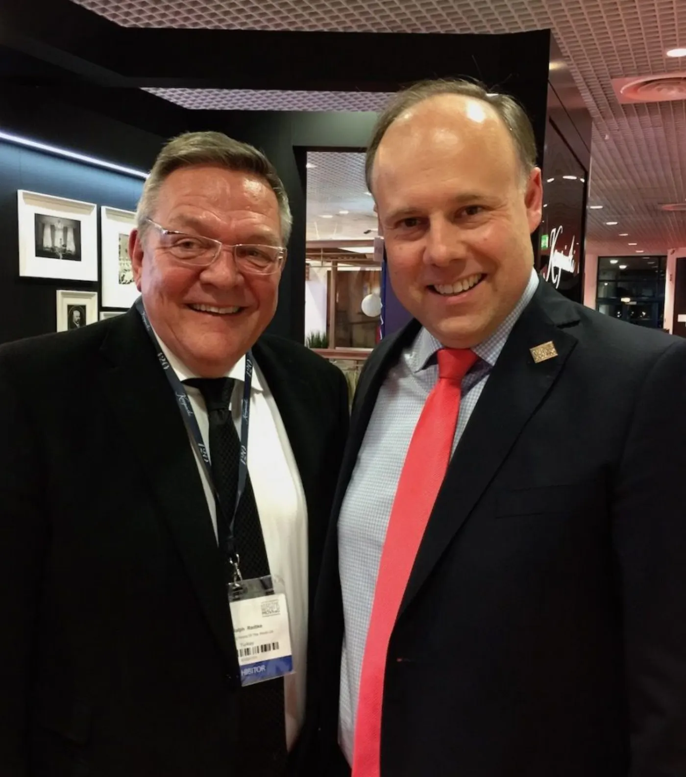Ralph Radtke, badge exposant au cou, souriant aux côtés d'un confrère en cravate rouge lors d'un salon professionnel