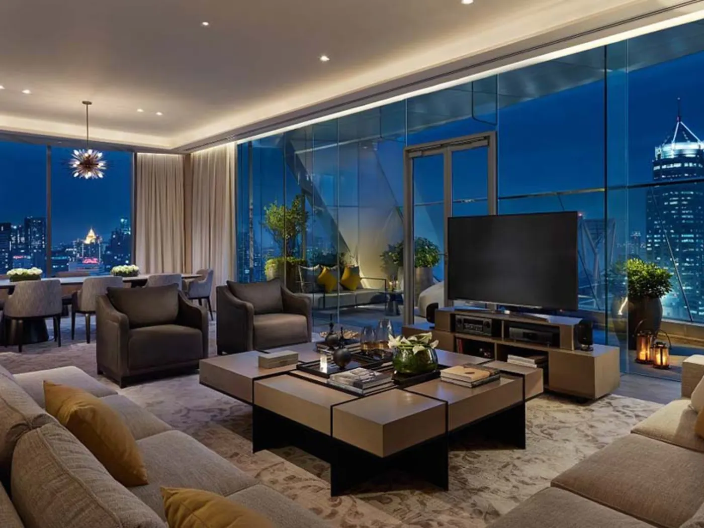Salon de suite aux baies vitrées ouvertes sur les tours illuminées de Bangkok à la nuit tombée