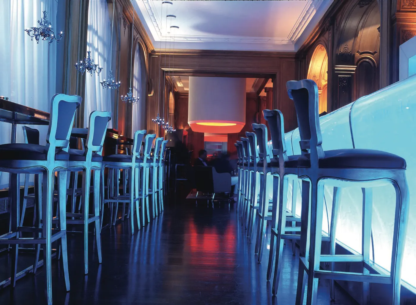 Bar du Plaza Athénée avec son comptoir de verre bleu lumineux, tabourets alignés et lustres en cristal