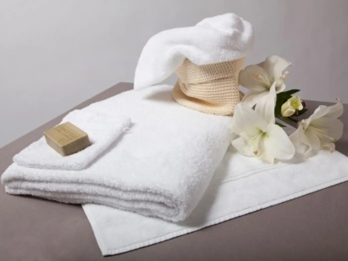 Serviettes de bain blanches pliées avec un savon vert, un gant, une panière en fibre et des fleurs blanches
