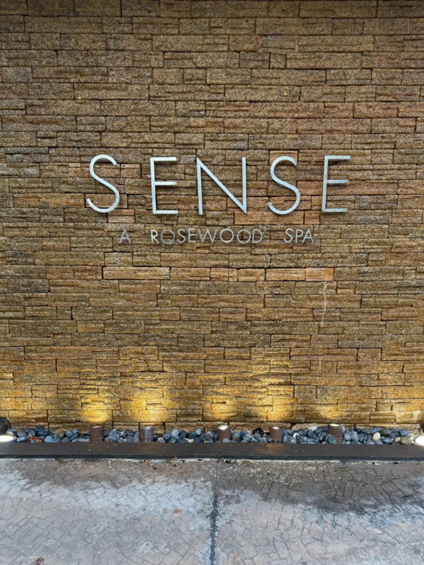 Enseigne métallique Sense, A Rosewood Spa fixée sur un mur de pierre éclairé par le bas