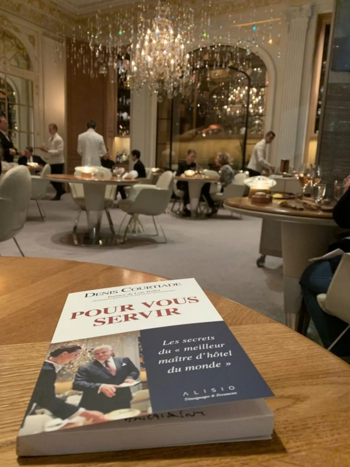 Le livre Pour vous servir posé sur une table ronde dans une salle de restaurant gastronomique à lustre de cristal