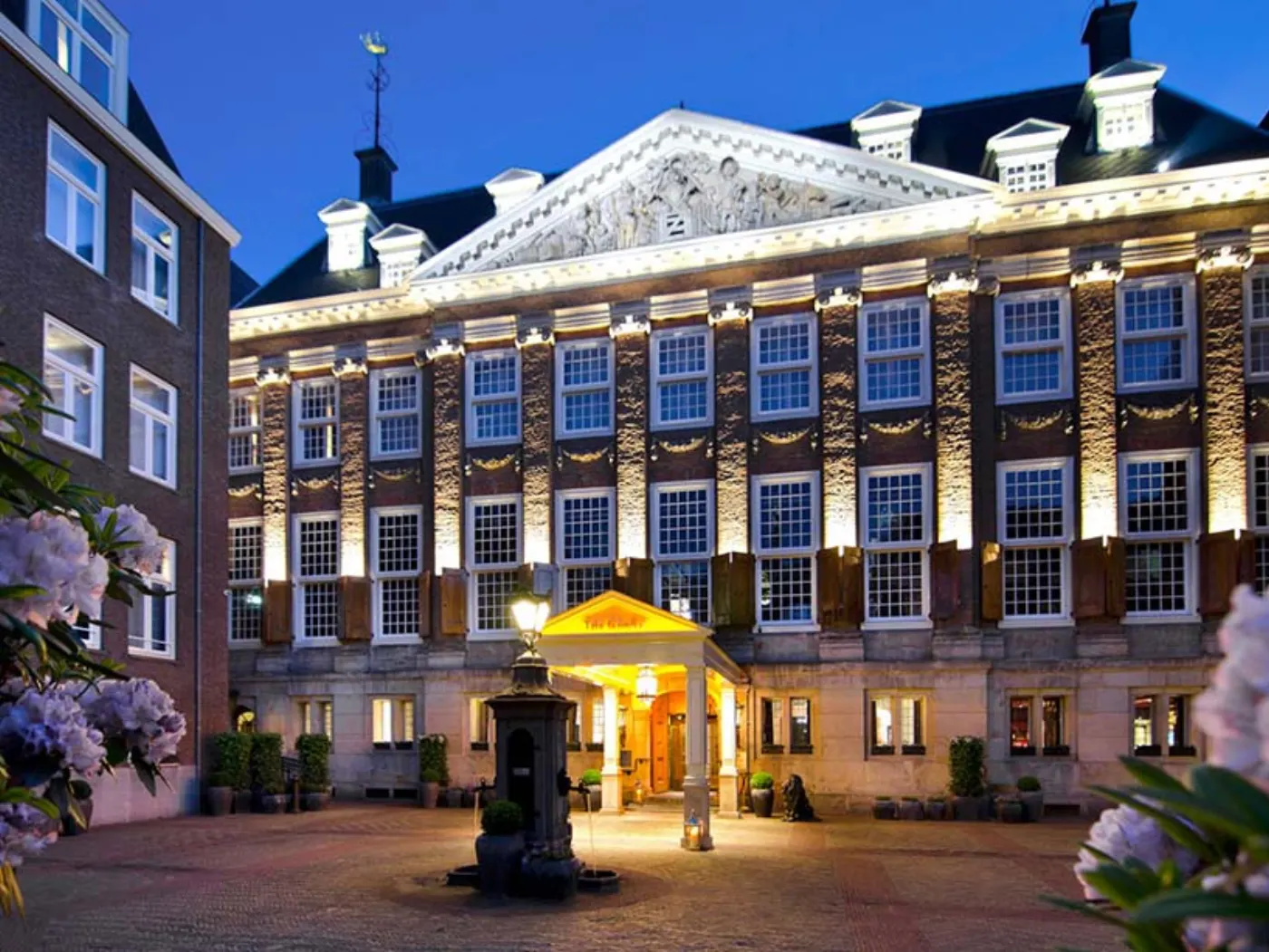 Façade classique du Sofitel Legend The Grand Amsterdam illuminée à la tombée du jour, avec sa cour pavée