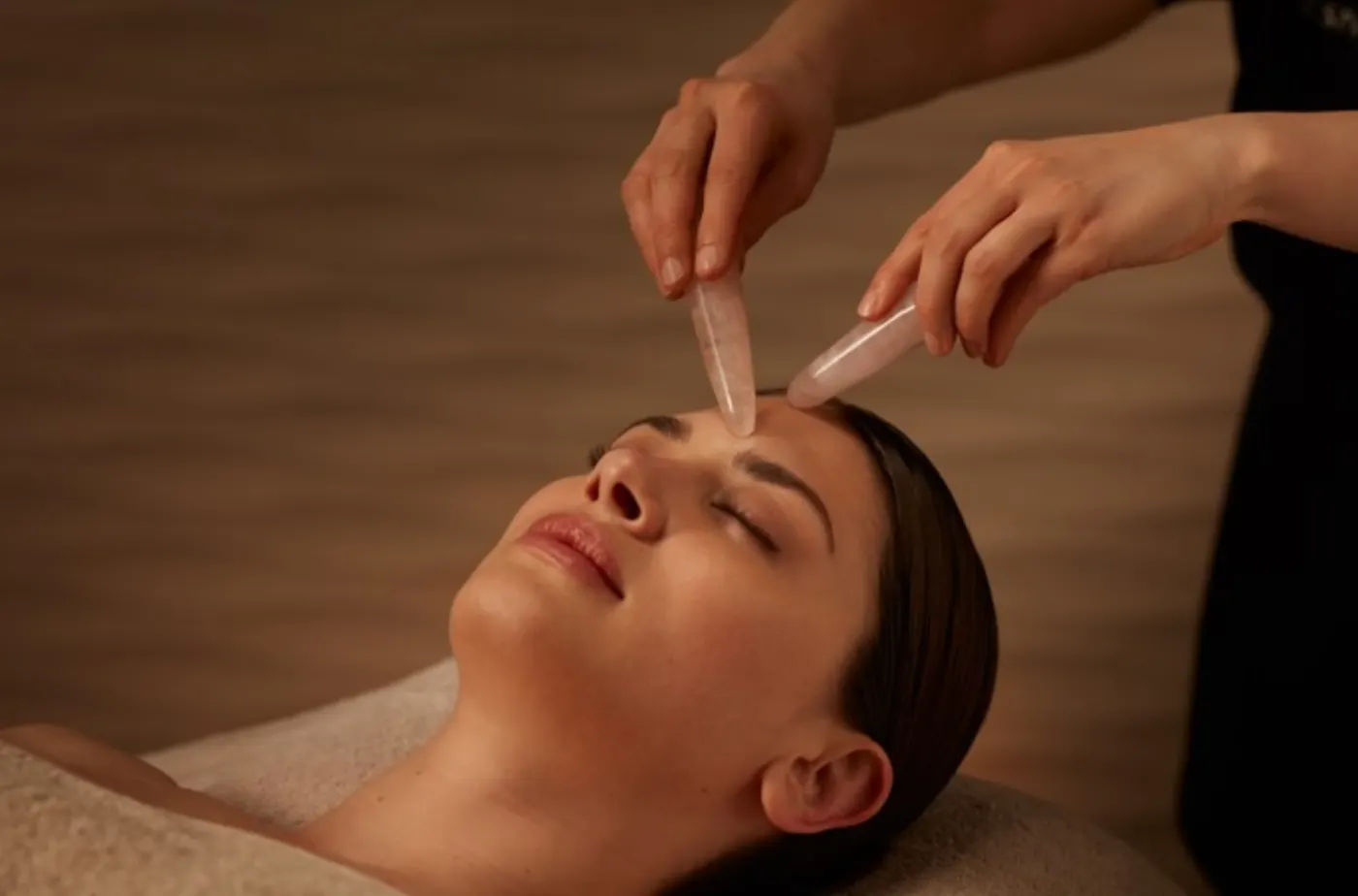 Femme allongée les yeux fermés recevant un soin du visage aux pierres de quartz rose sur le front