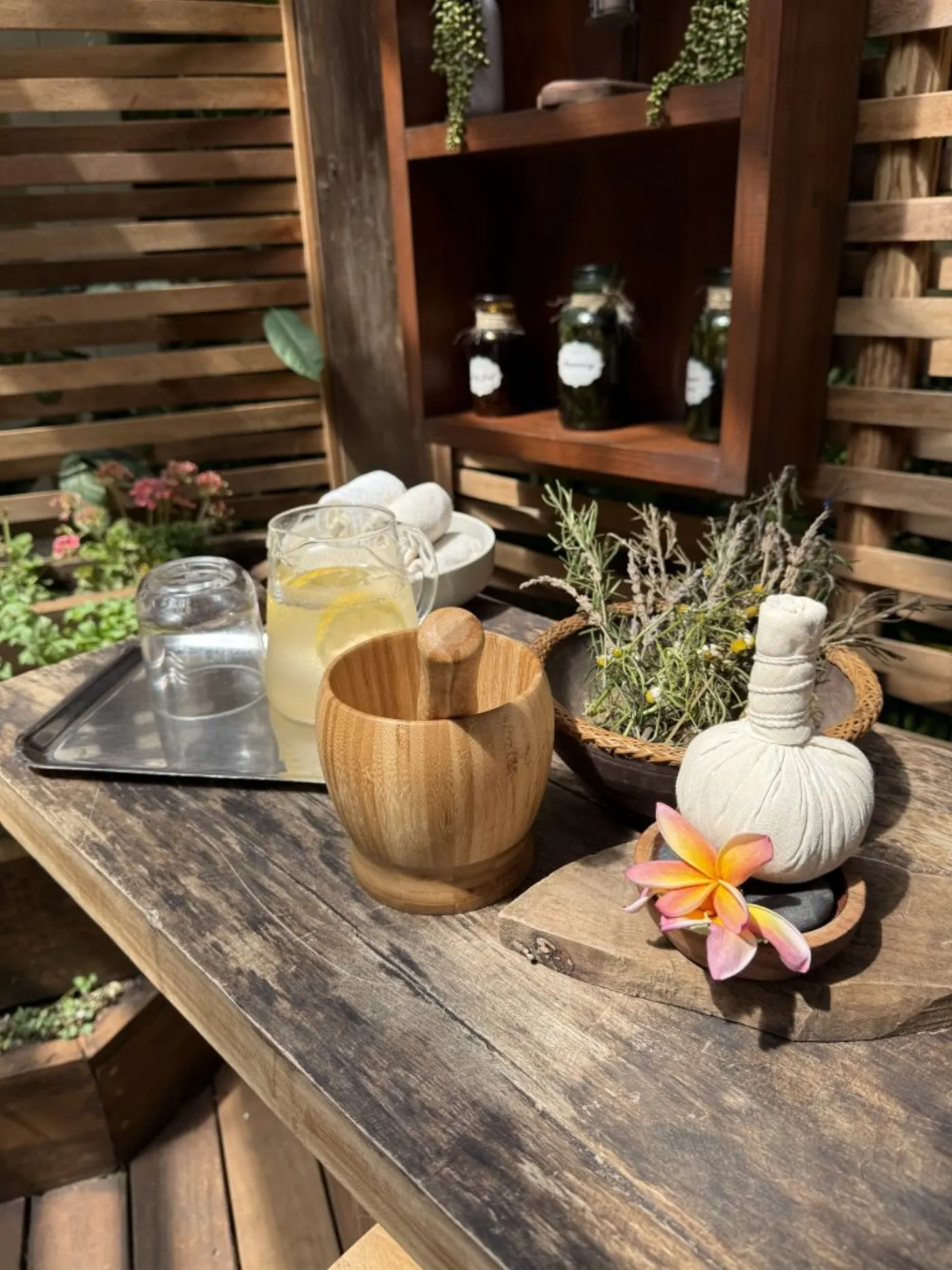 Table en bois d'un spa: carafe d'eau citronnée, mortier en bambou, baluchon de plantes et fleur de frangipanier