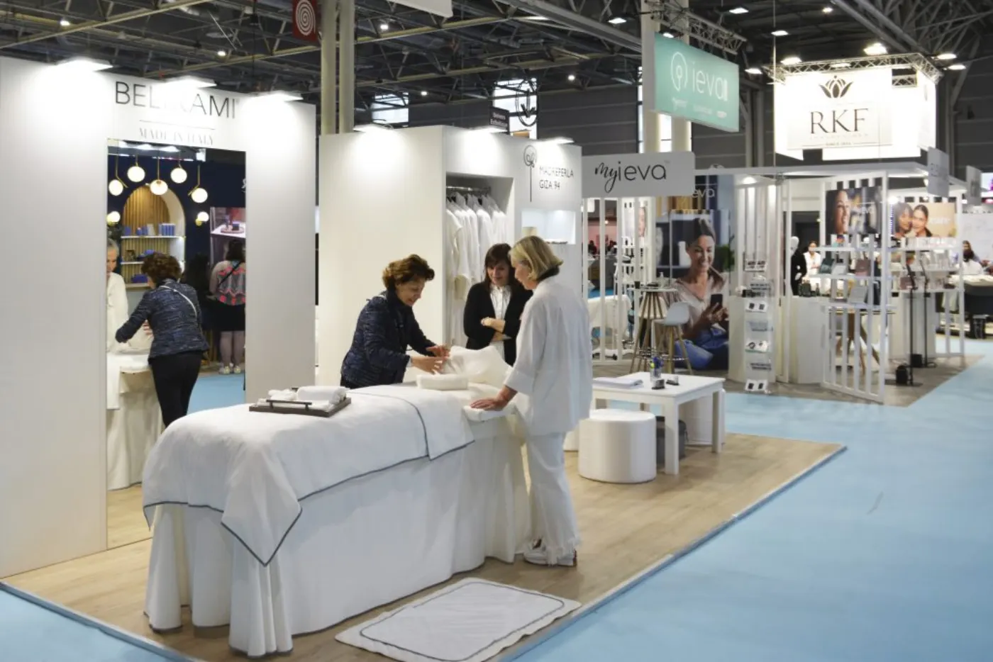Stand de salon professionnel avec table de massage habillée de blanc et trois femmes en discussion