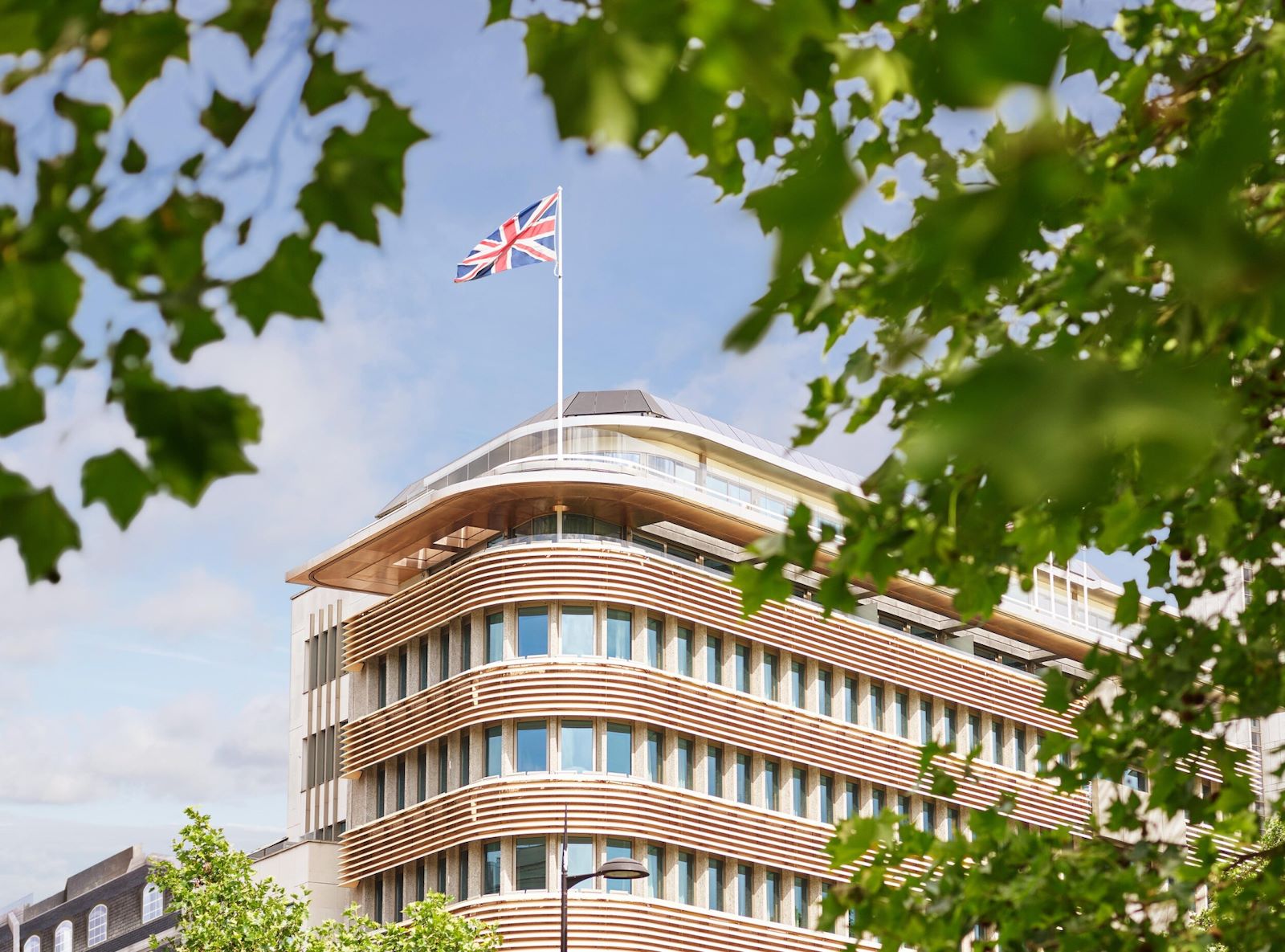 Façade de l’hôtel 45 Park Lane à Londres, bandeaux de bois courbes sous un drapeau britannique, à travers le feuillage