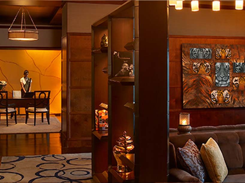 A Leela Palace lounge: warm wood panelling, a tiger canvas and a receptionist at the desk beyond