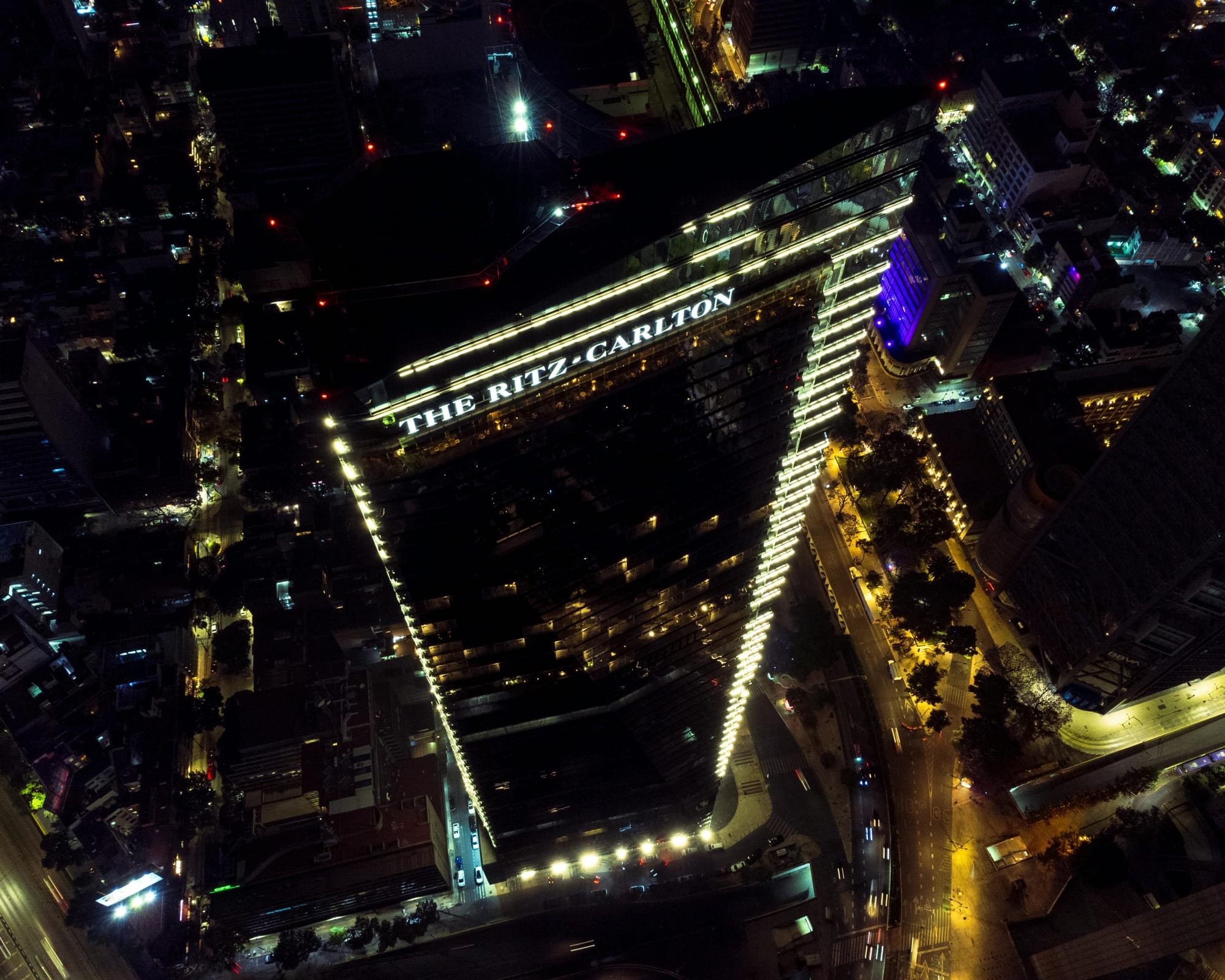 Tour Ritz-Carlton vue du ciel la nuit, son enseigne lumineuse dominant les avenues éclairées