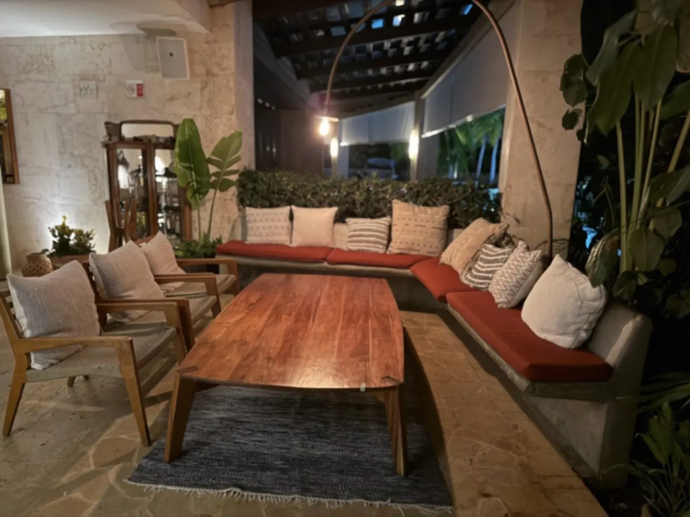 Salon extérieur du Rosewood Mayakoba : banquette à coussins rouges, table de bois et lampe arquée