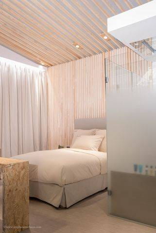 La Chambre ORIGINE® à EquipHotel 2016 : lit aux draps blancs, parois en lames de bois et salle de bains vitrée