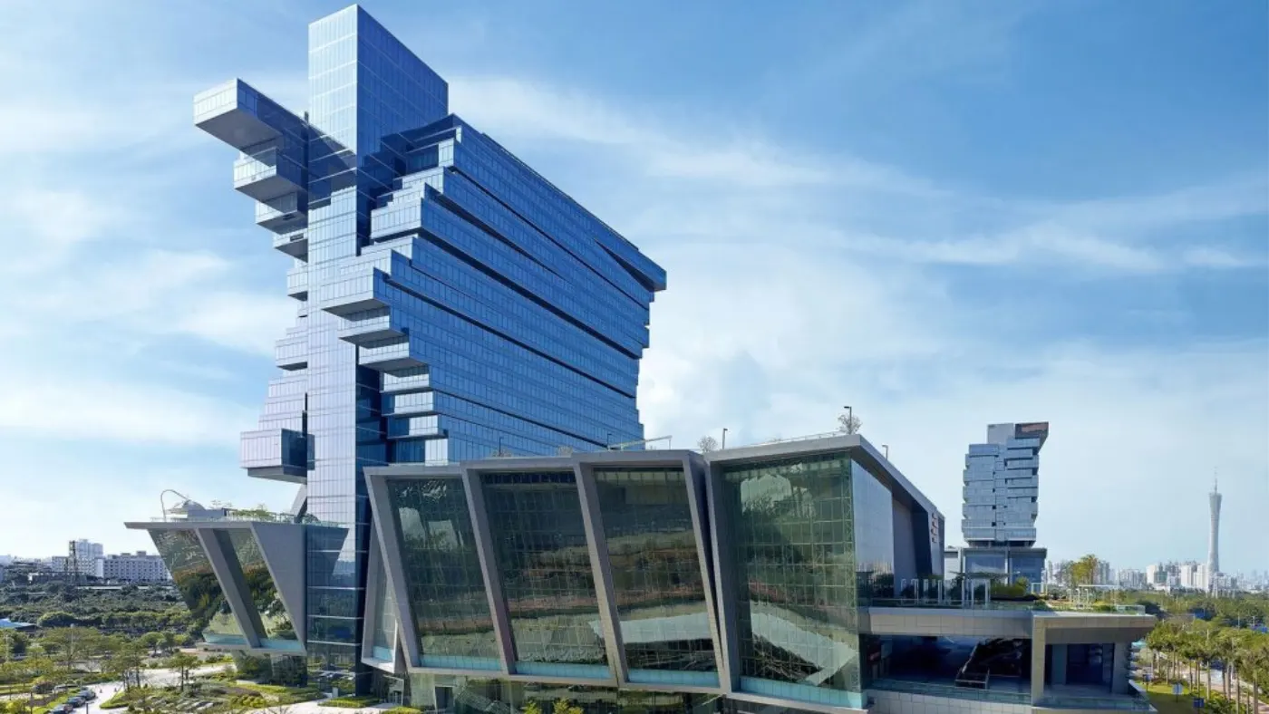 Tour de verre contemporaine aux volumes en porte-à-faux, podium vitré incliné et skyline d'une grande ville au loin