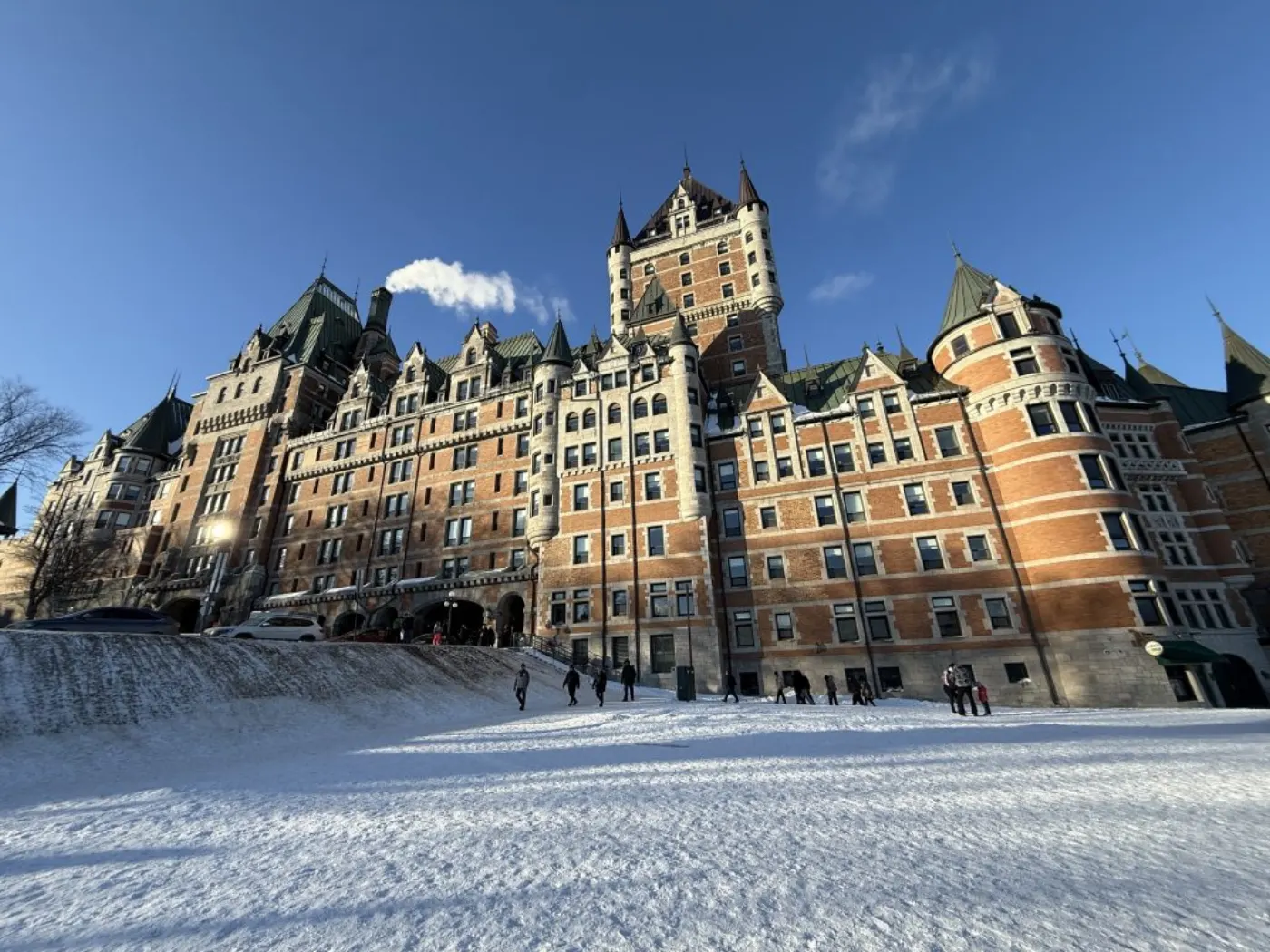 Fairmont Le Château Frontenac from below under a blue winter sky, walkers on the snow-covered terrace
