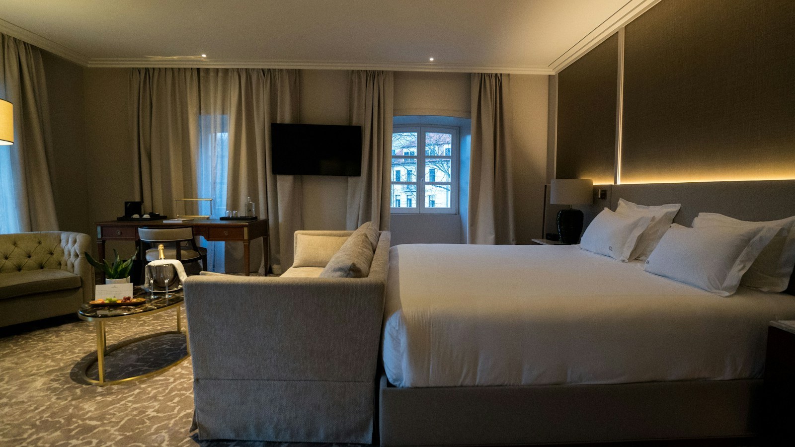 Luxury hotel room with a large bed, a sitting area and a work desk, illustrating plural hospitality and the many uses of a single room