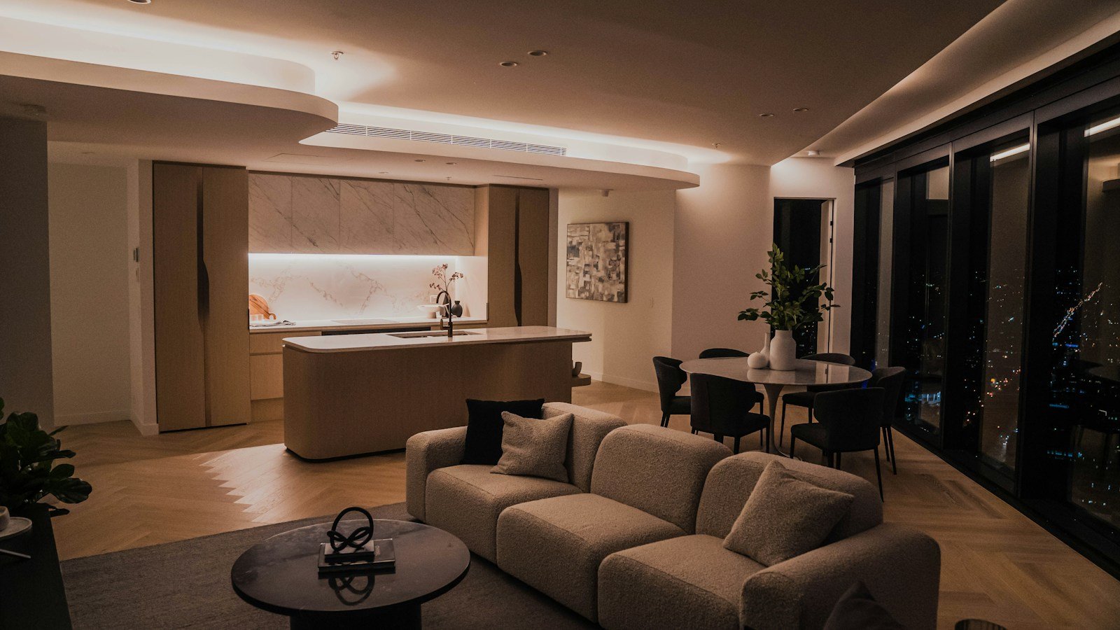 Luxury suite with an open kitchen, living room and dining area opening onto a night view of the city, designed for long stays
