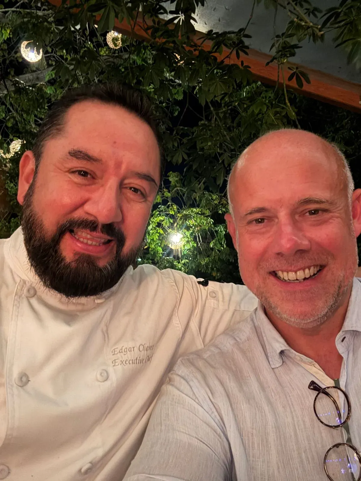 Laurent Delporte et le chef Edgar Chávez, en veste de cuisine, souriants, sous les lumières du jardin du Rosewood Mayakoba