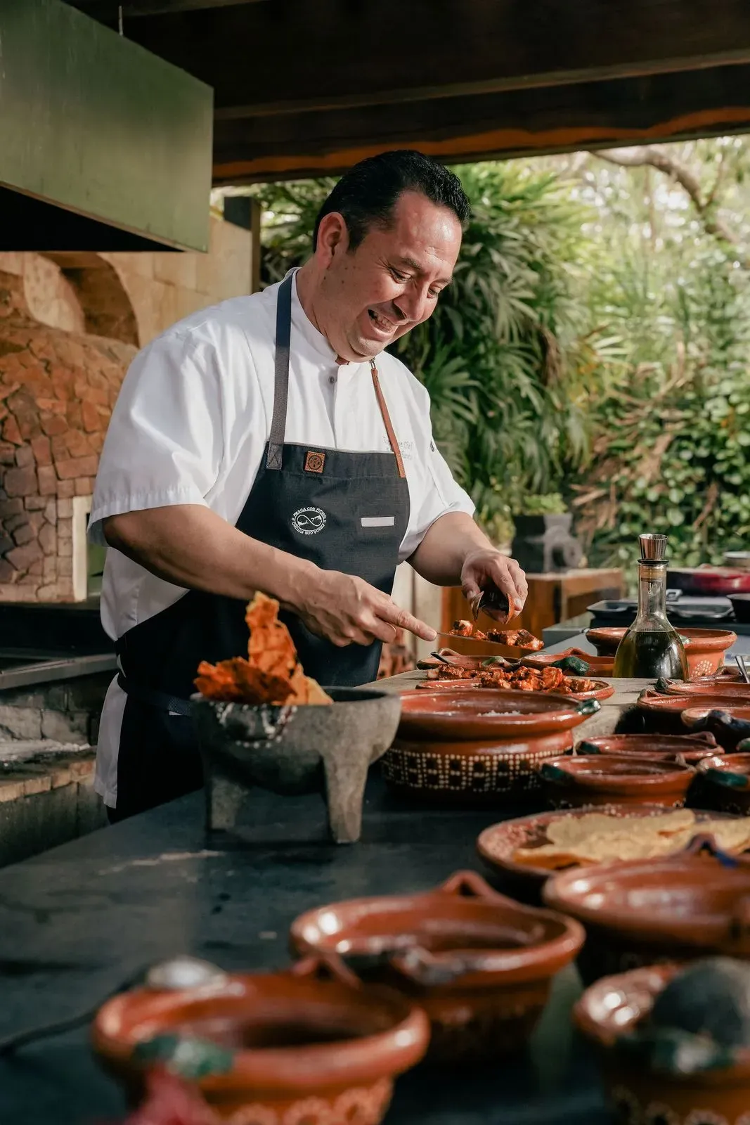 Le chef Edgar Chávez sourit en préparant un plat devant le four traditionnel maya, entouré de poteries en terre cuite