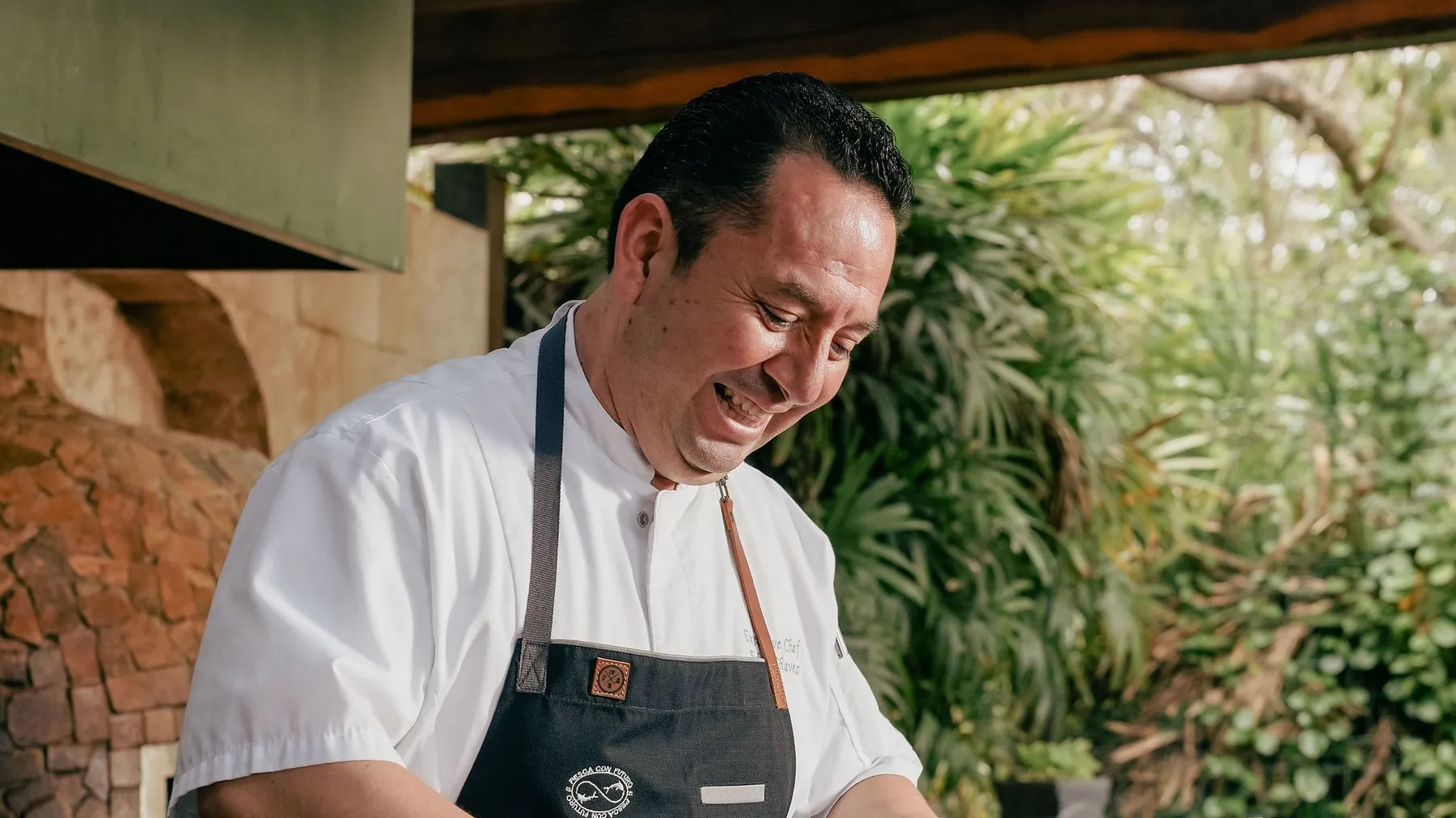 Le chef Edgar Chávez sourit en cuisinant devant le four traditionnel maya du Rosewood Mayakoba
