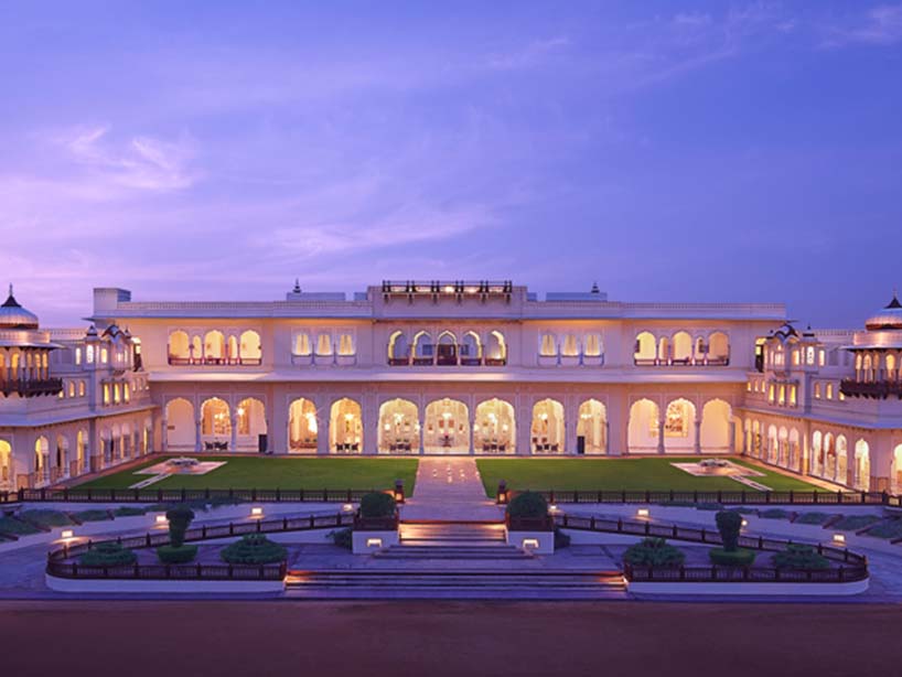 An illuminated Taj palace at dusk, its arcades and lawns beneath a violet sky
