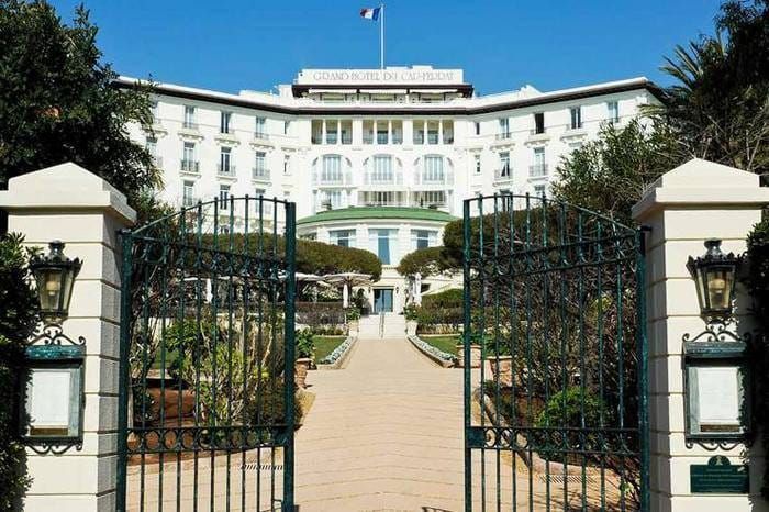 Grille ouverte du Grand-Hôtel du Cap-Ferrat, l'allée menant à la façade blanche et au drapeau
