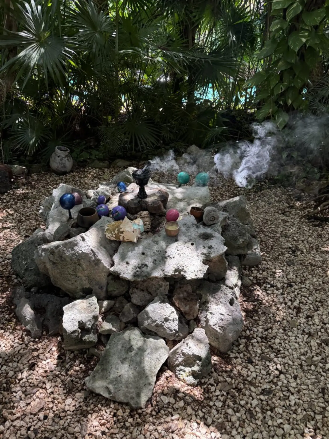 Autel de pierre garni de sphères colorées, coquillages et coupelles, avec de la fumée d'encens dans la jungle