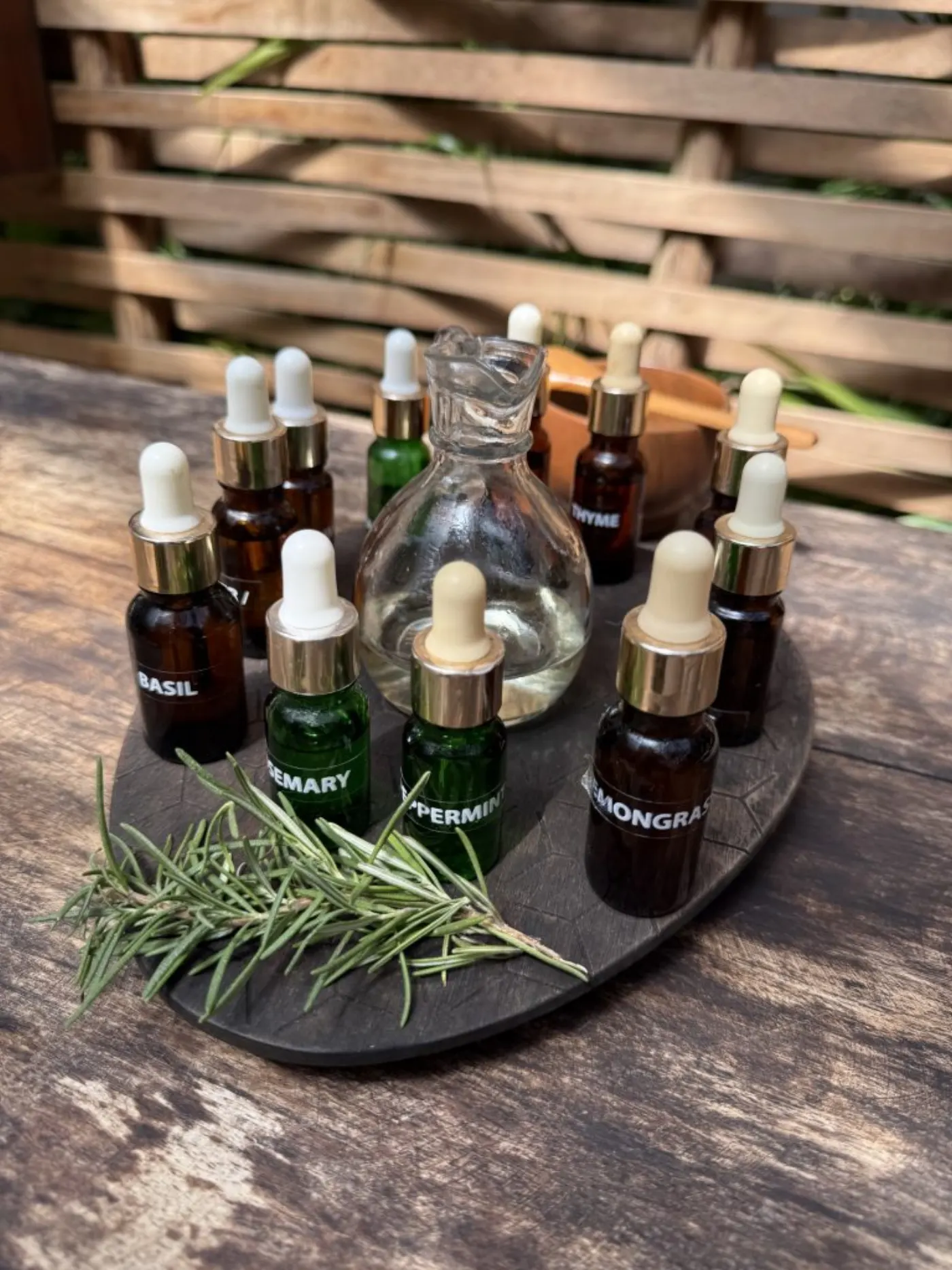 Flacons d'huiles essentielles (basilic, romarin, menthe, citronnelle) autour d'un flacon en verre, avec un brin de romarin