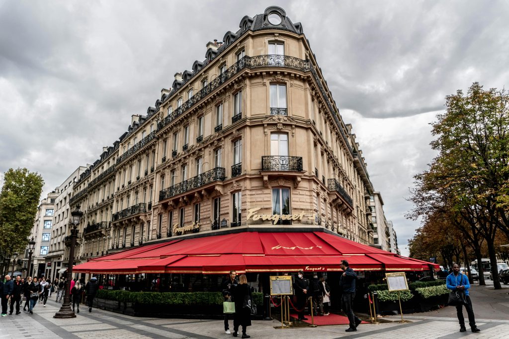 Charming Parisian restaurant with red awnings and classic architecture under a cloudy sky.